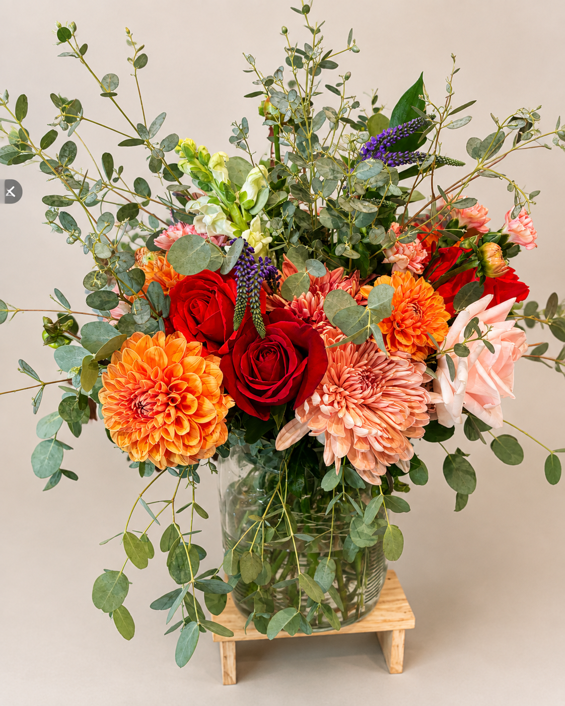 Custom floral arrangement featuring orange dahlias, red roses, peach chrysanthemums, purple veronica, and eucalyptus.