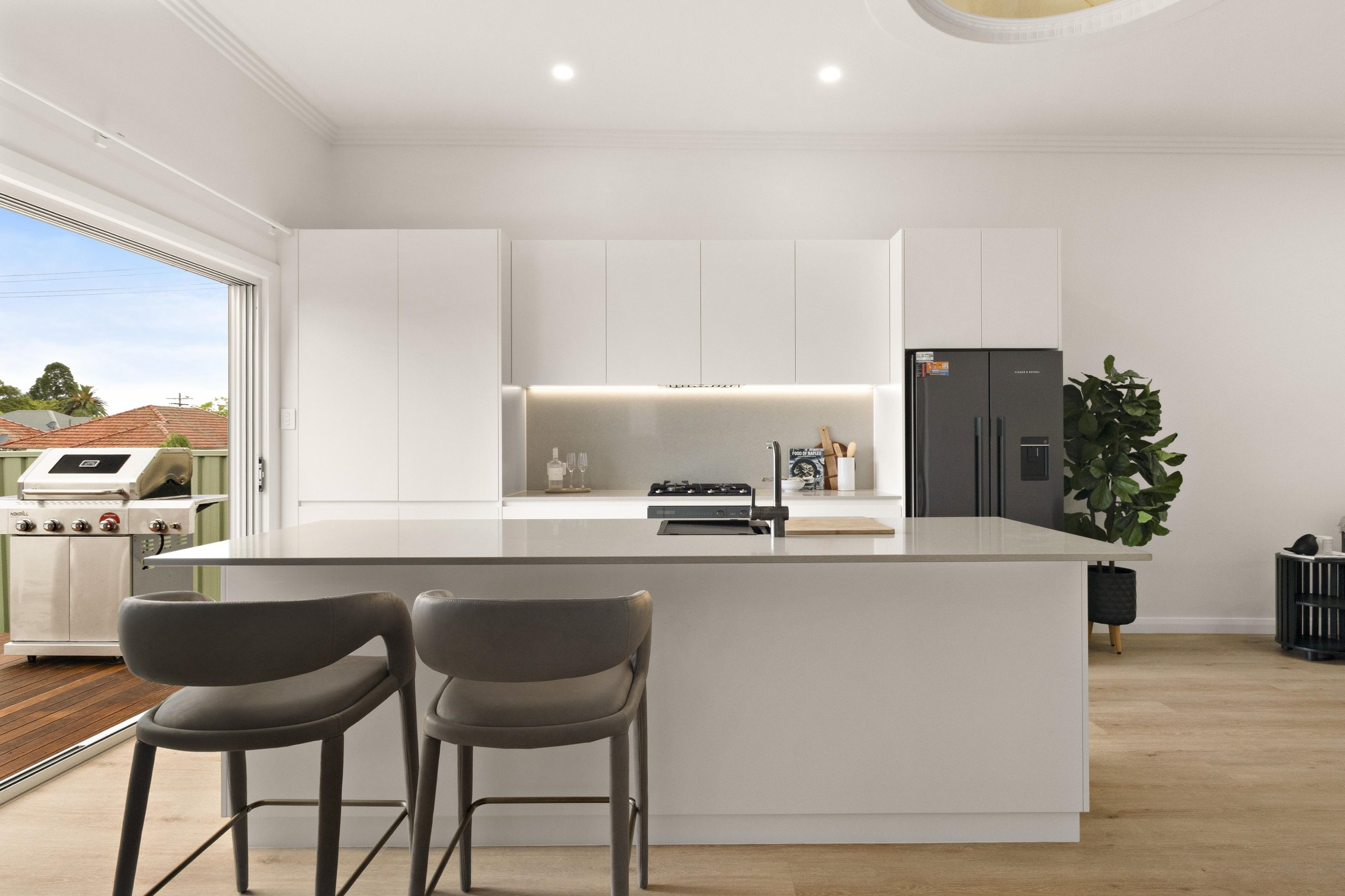 Modern kitchen with white cabinets, a large island with a sink, a black refrigerator, and a sliding glass door leading to an outdoor patio.
