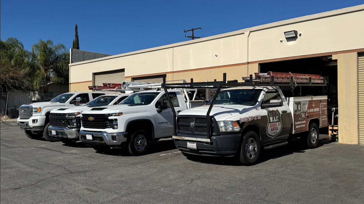 Four white service trucks parked in a lot outside a commercial building with closed garage doors.