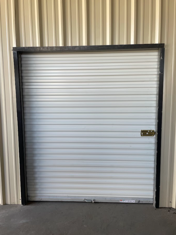 A white roll-up garage door with a black frame, installed in a beige metal building.