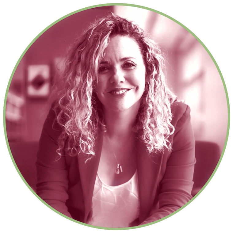A woman with curly hair smiling at the camera, sitting indoors with a blurred background, edited with a pinkish filter.