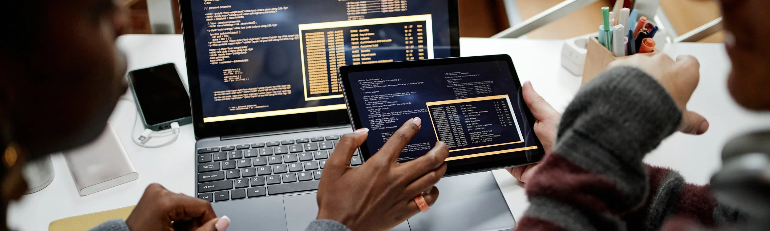 Students reviewing and testing code on a laptop and tablet during a collaborative programming session.