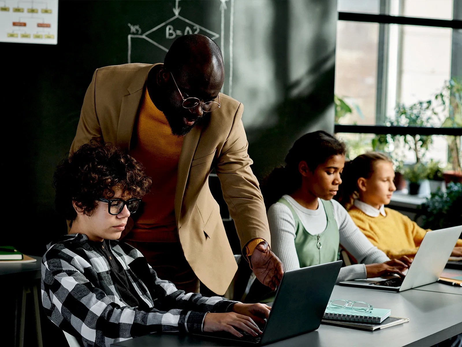 Instructor mentoring students working on laptops during a technology learning session