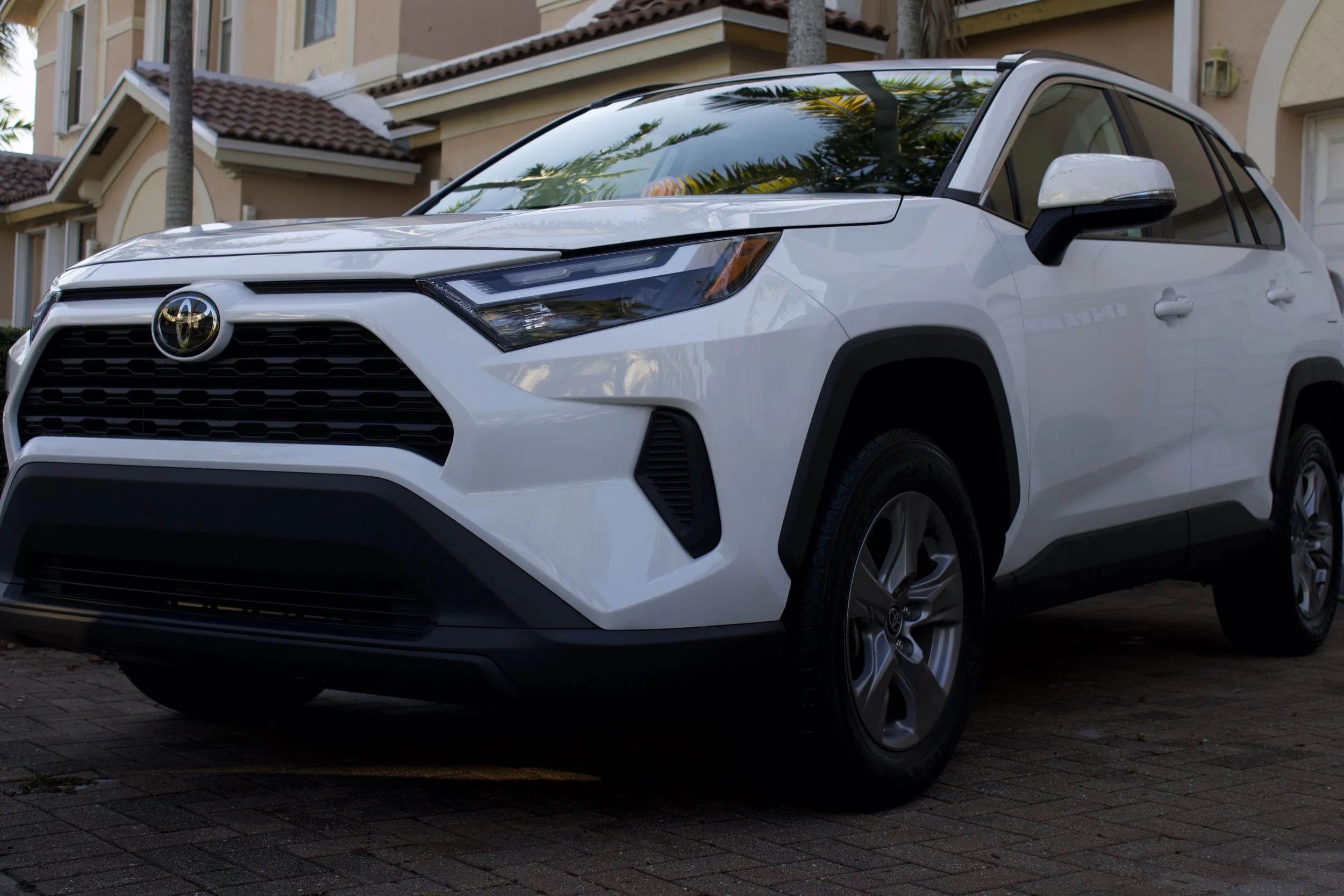 White Toyota SUV parked on a brick driveway in front of residential houses with palm trees.