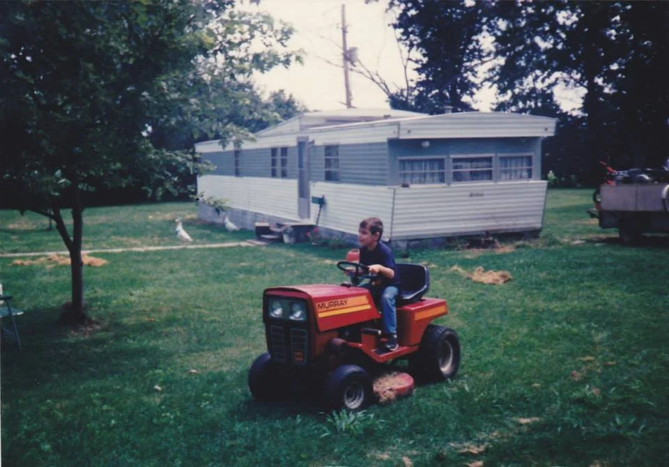 Me riding a red tractor, in front of a mobile home