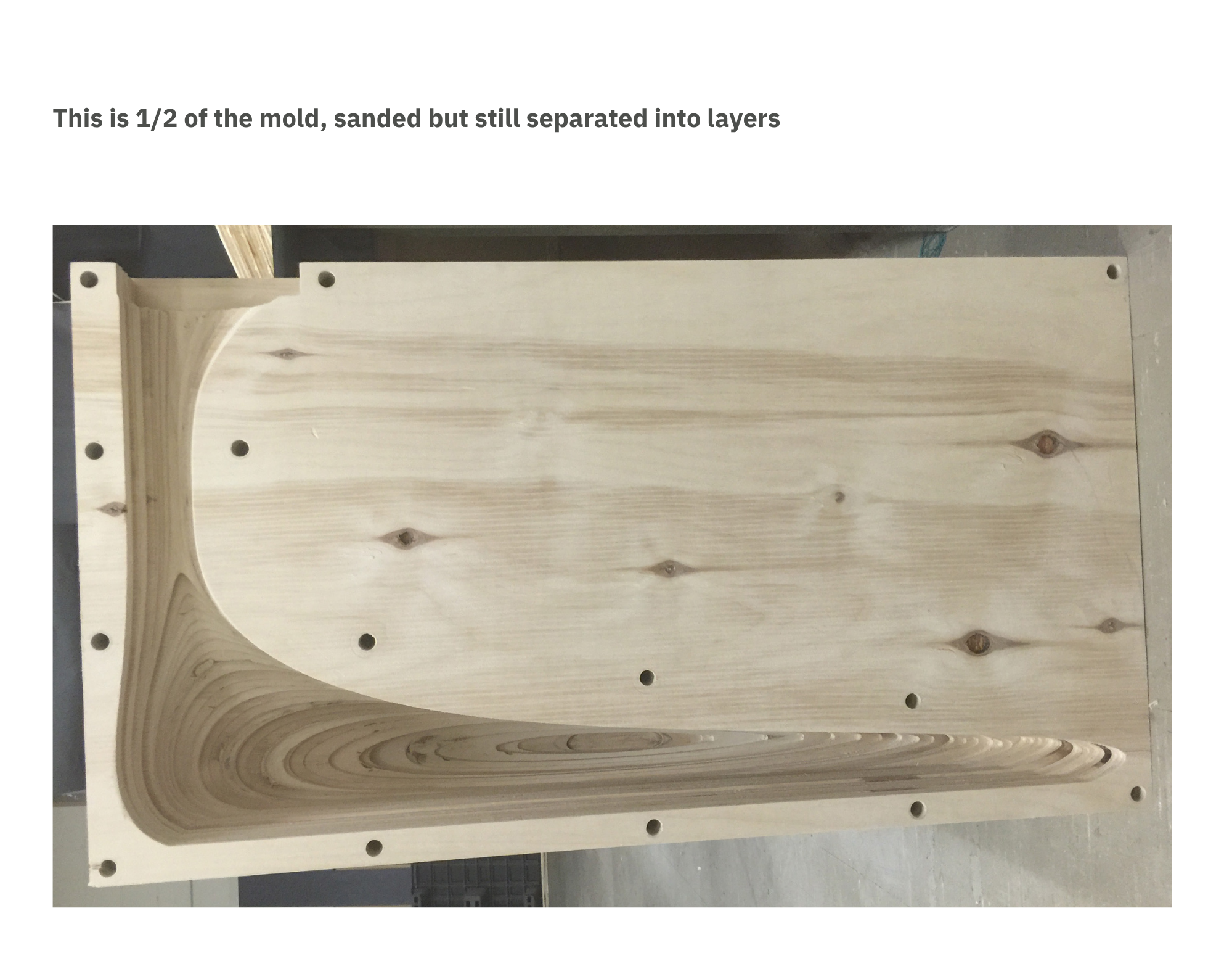 A wooden mold with drilled holes, sanded but still divided into layers, resting on a workbench in a woodworking shop.
