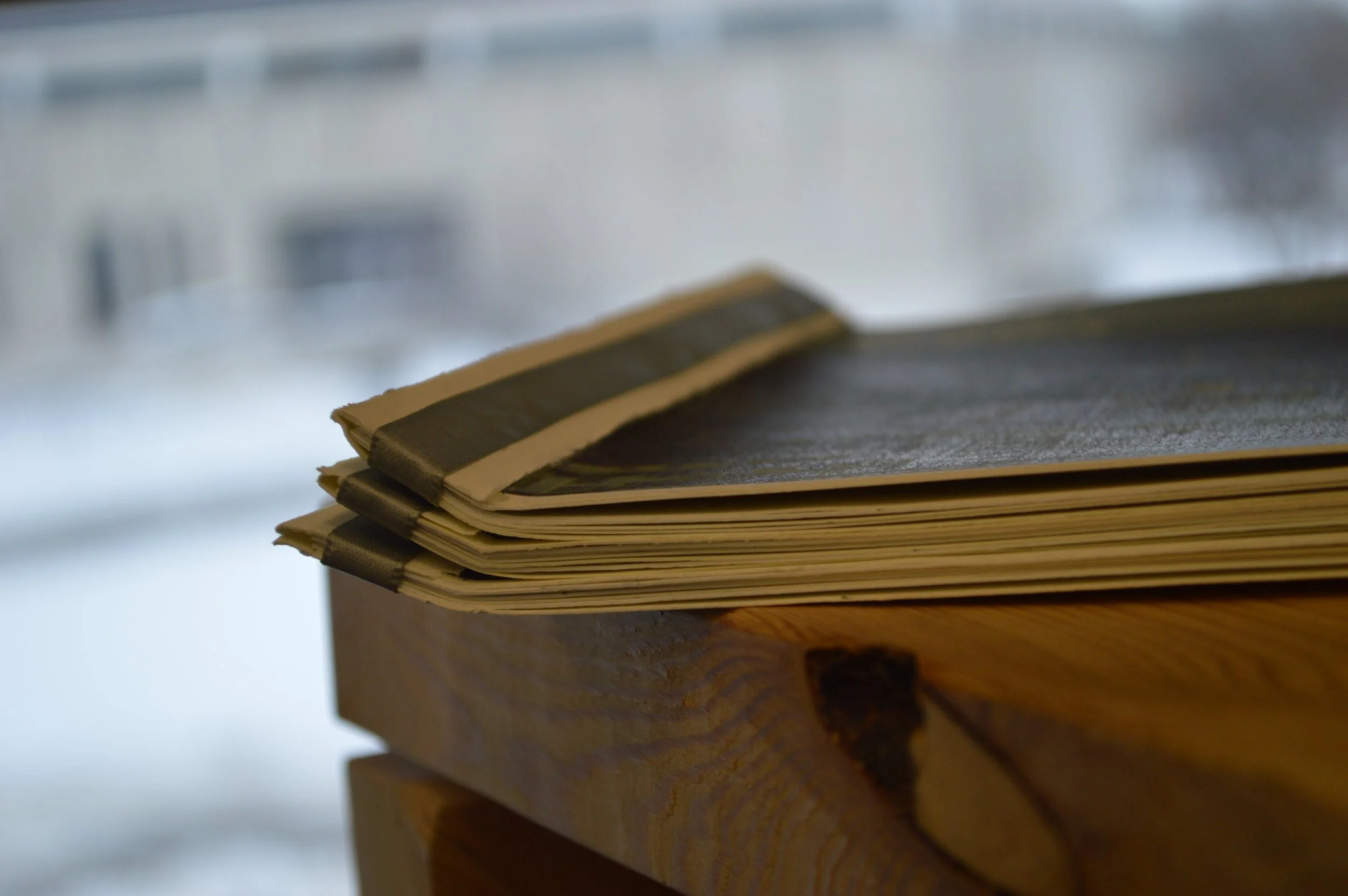 A stack of folded magazines or newspapers on a wooden surface with a blurred background.