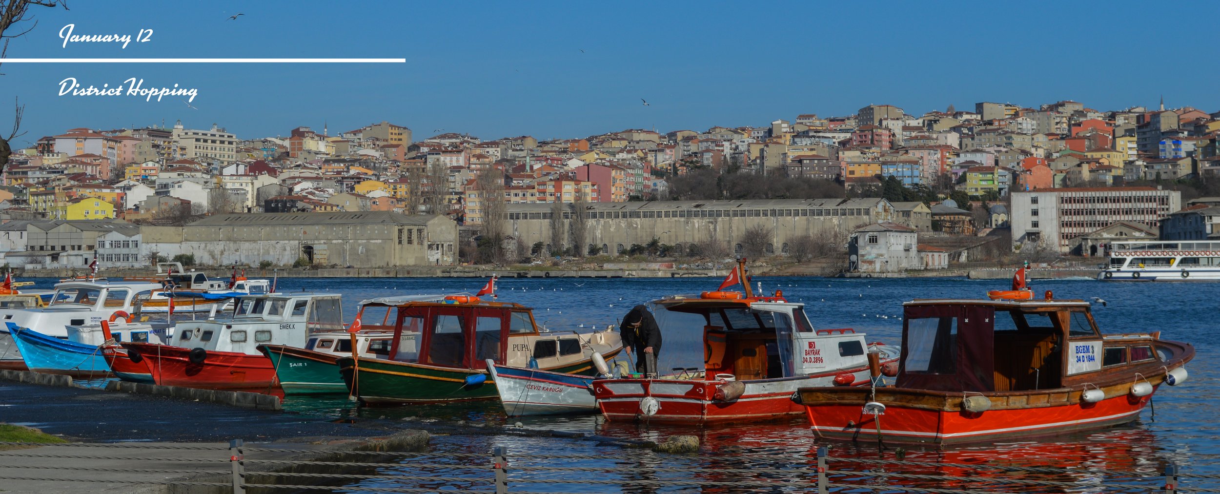 Boats docked on a river with a cityscape of colorful buildings on a hillside in the background on a clear day with blue sky.