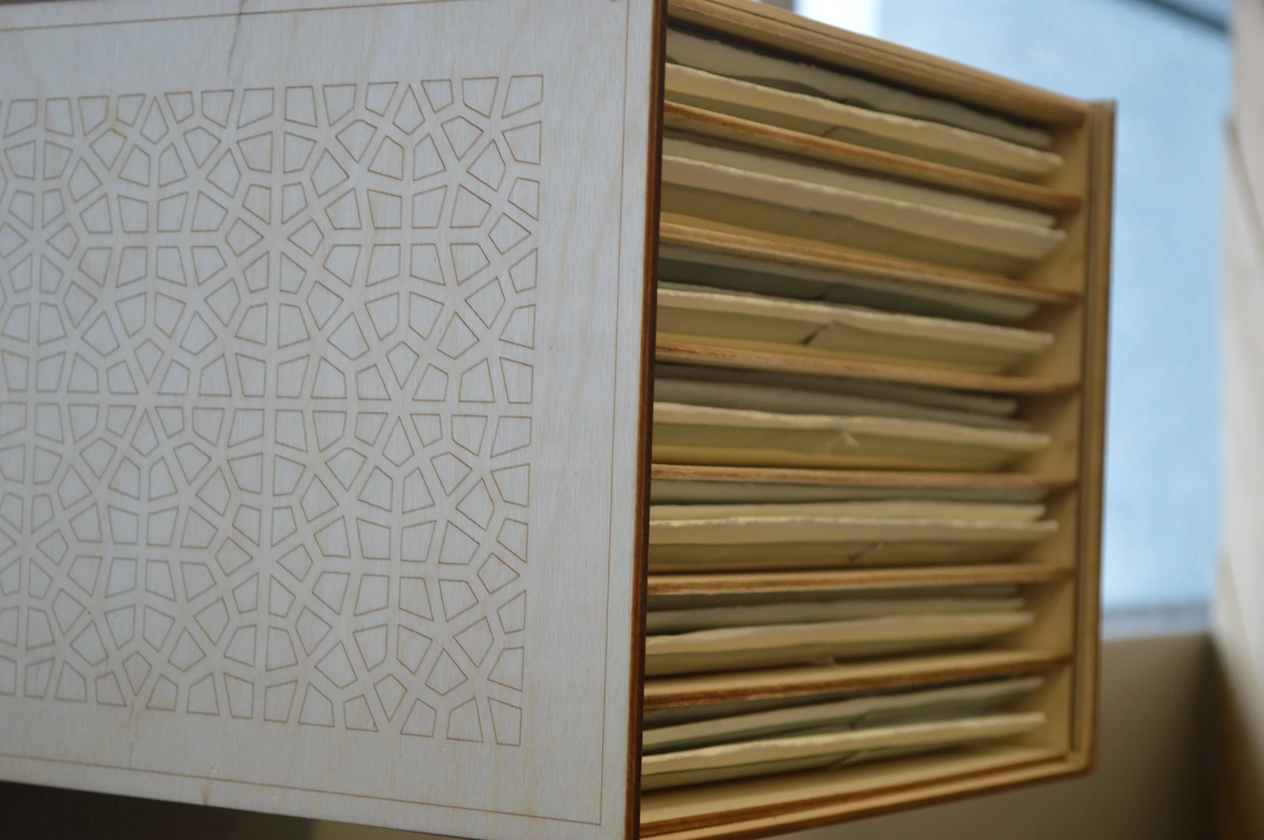 Close-up of a wooden file rack with multiple hanging folders, partially obscured by a decorative wooden panel with an intricate geometric cutout pattern.