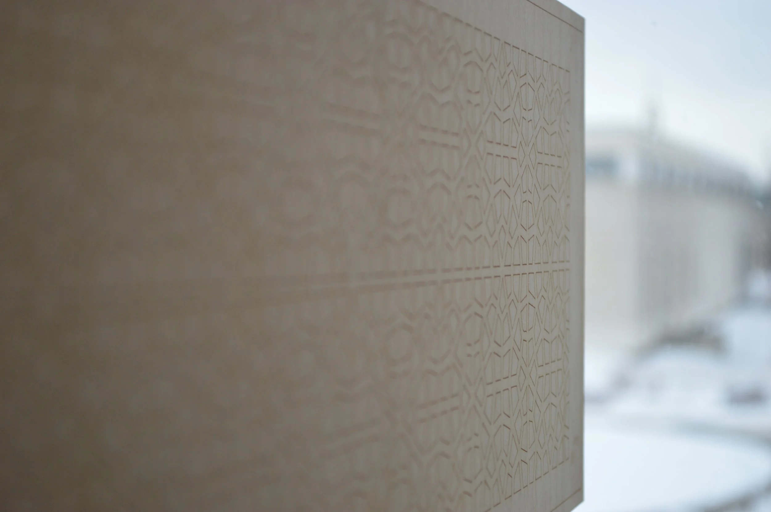 Close-up of a beige wall with a geometric etched pattern, partially blurred background with bright light.