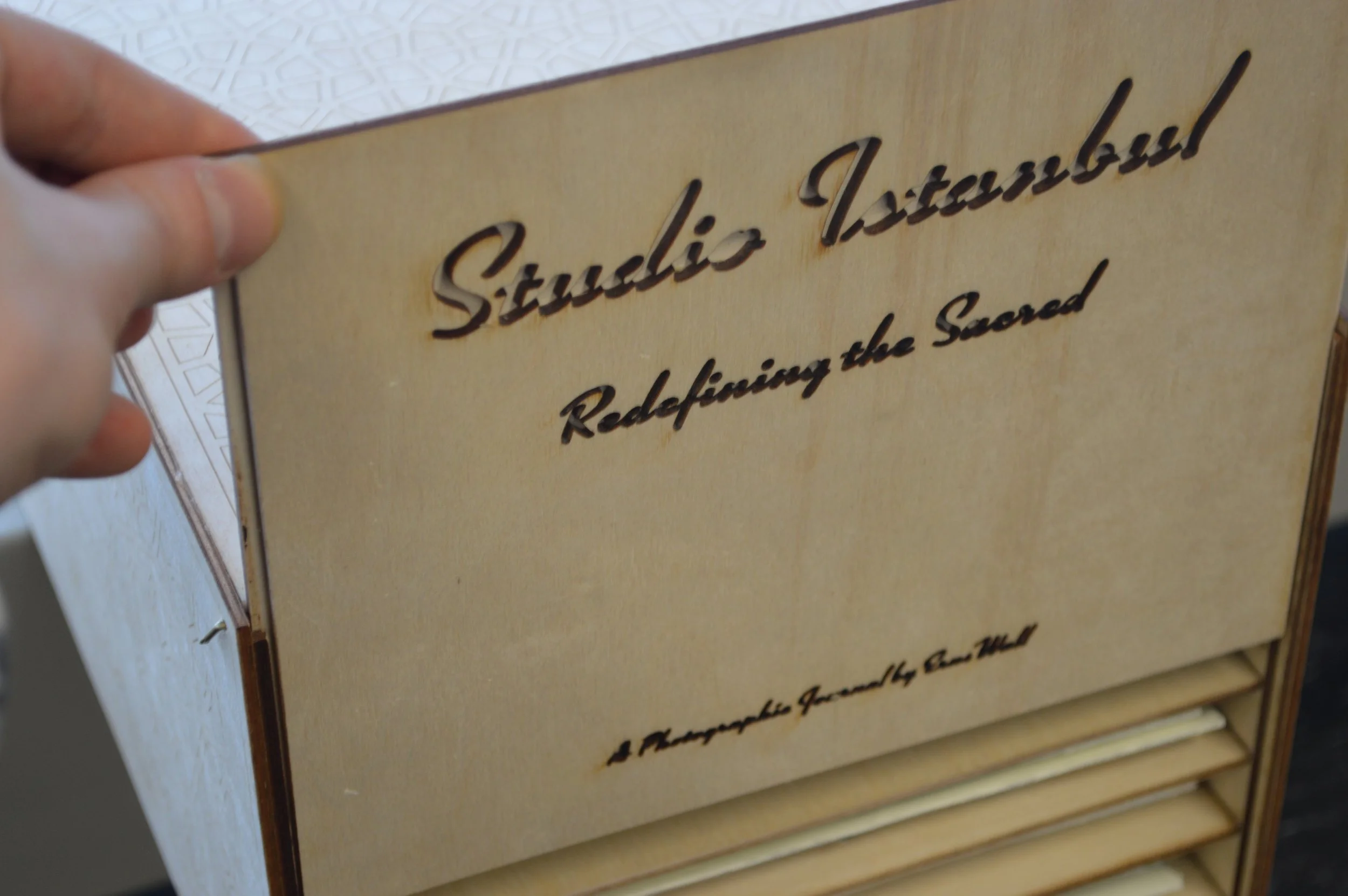 Close-up of a person holding a beige-colored sign or plaque with the words 'Studio Architectural' inscribed in cursive, along with additional text that is partially visible.