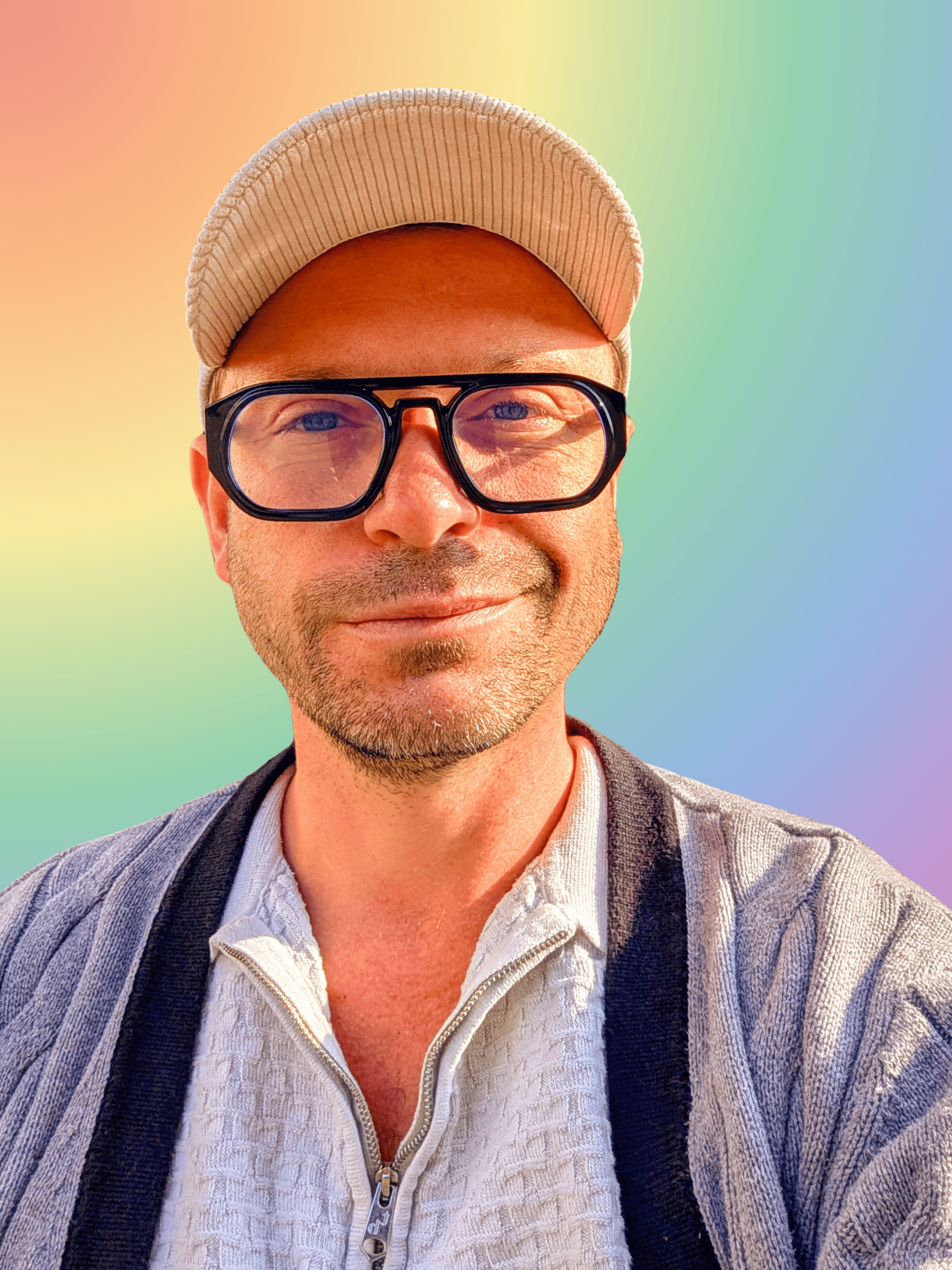 A man wearing a beige baseball cap, black glasses, a white textured zip-up sweater, a striped blazer, and a shoulder bag, smiling in front of a colorful gradient background.