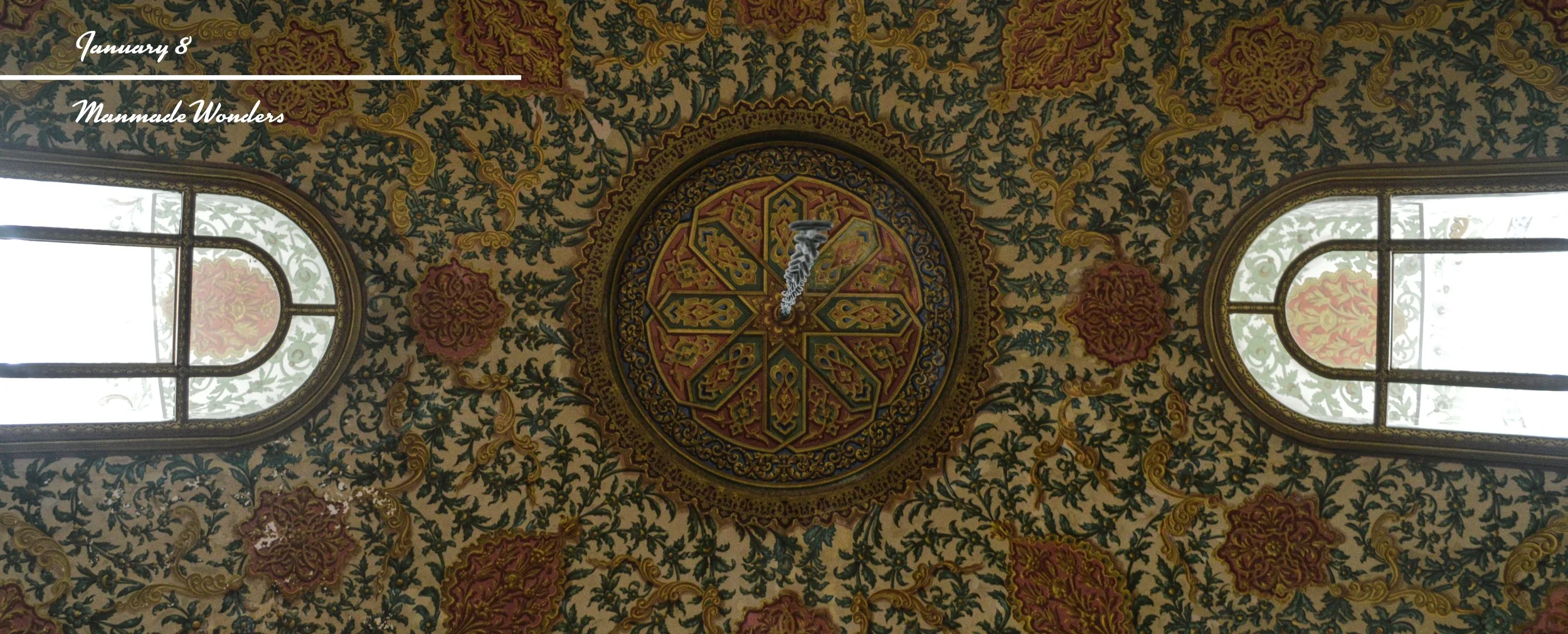 Decorative ceiling with intricate floral and gold patterns, two arched stained glass windows, and a circular ornamental design in the center.