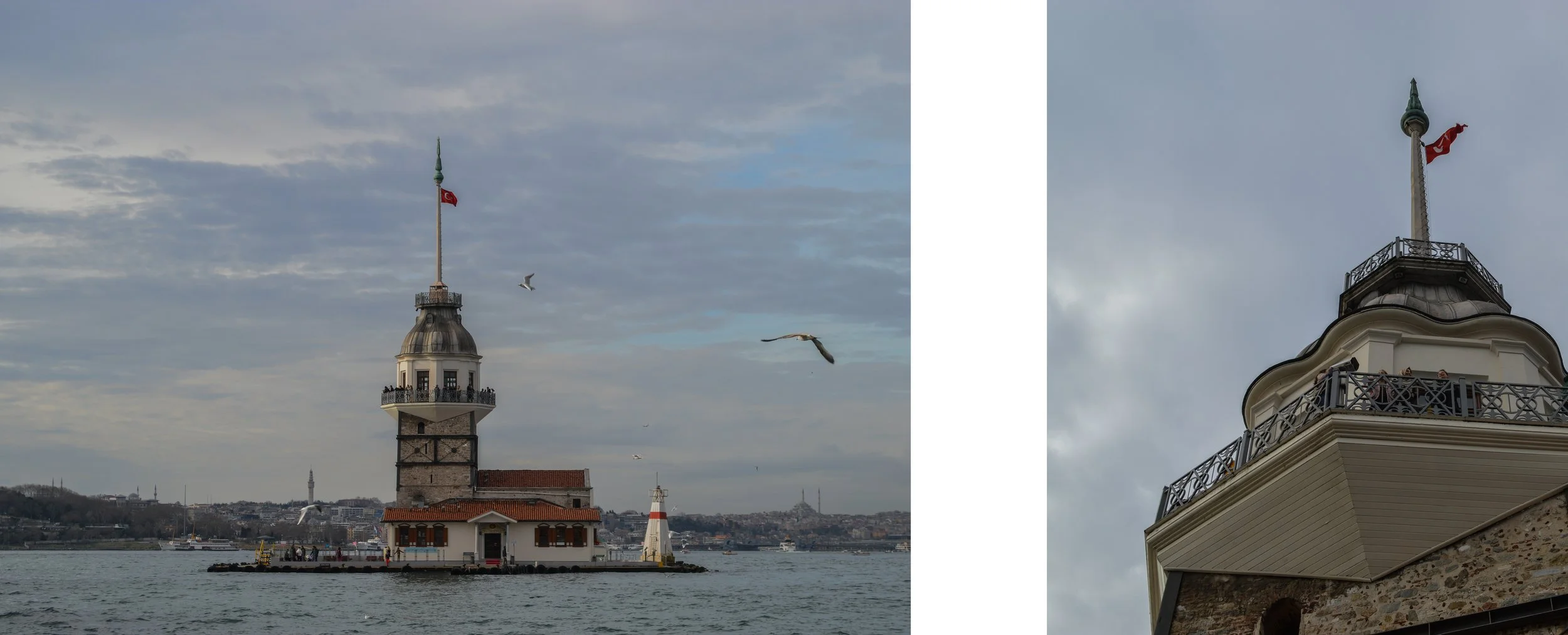A historic lighthouse with a Turkish flag on top, located on a small island in a body of water, with a city skyline and hills in the background. The photo also shows seagulls flying near the lighthouse.