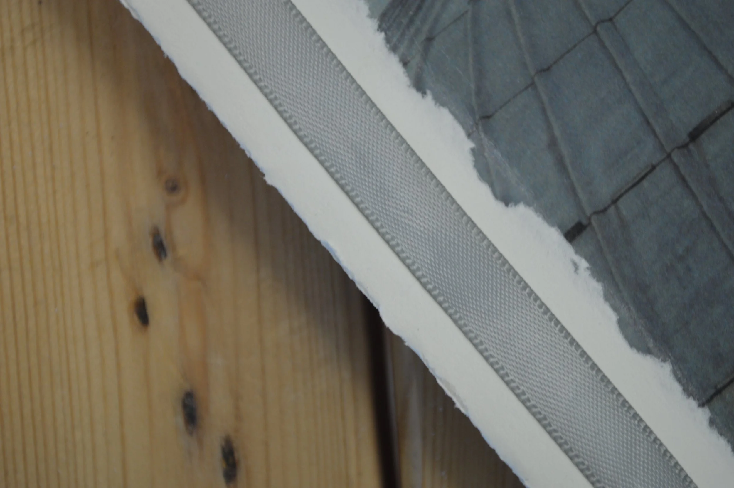Close-up of a section of a wall showing the intersection of gray stone tiles with white drywall, and a metal drywall corner bead, on a wooden surface background.