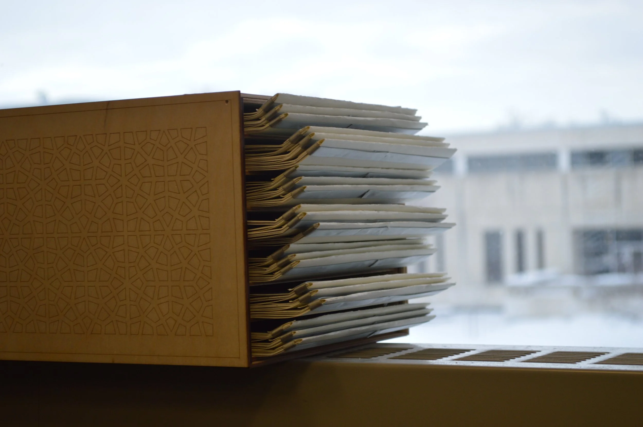 A wooden file organizer holding multiple files with paper tabs, placed in front of a window with a cityscape view of buildings.