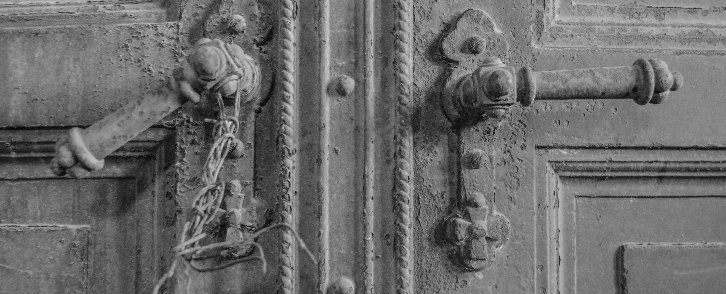 Close-up of an old, rusty metal door latch with a chained and padlocked handle.