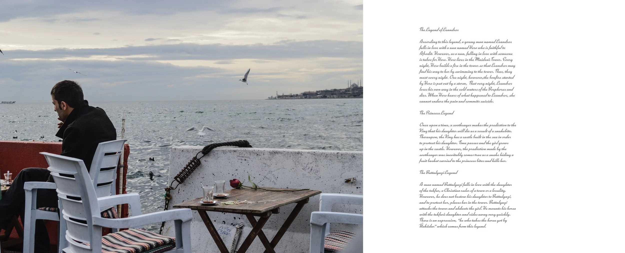 A man sitting on a white chair by the water, with a table and planes in the background, seagulls flying over the sea on an overcast day.