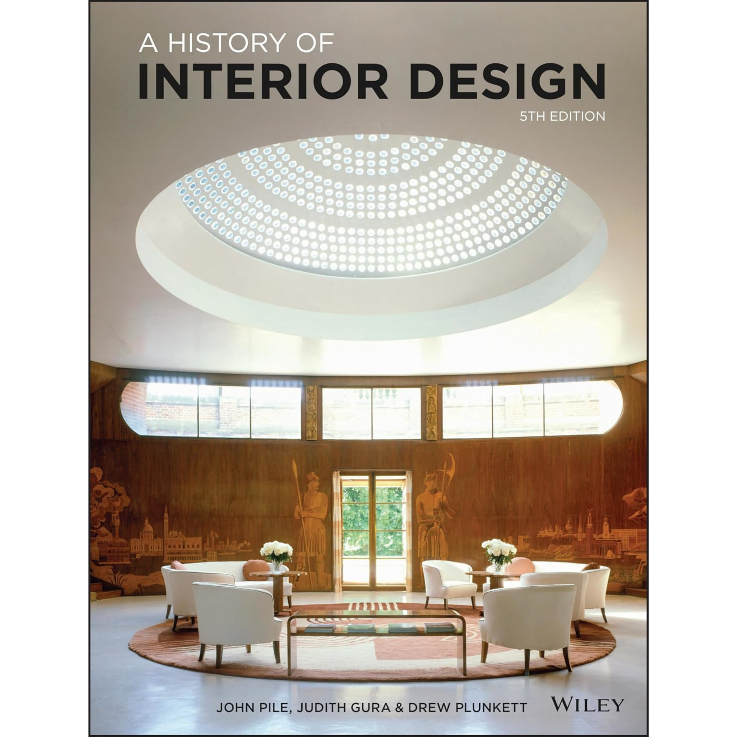 Book cover titled "A History of Interior Design, 5th Edition" published by Wiley. The background shows a well-lit interior with large windows, wooden wall paneling with decorative carvings, and a sitting area with white chairs and round tables.