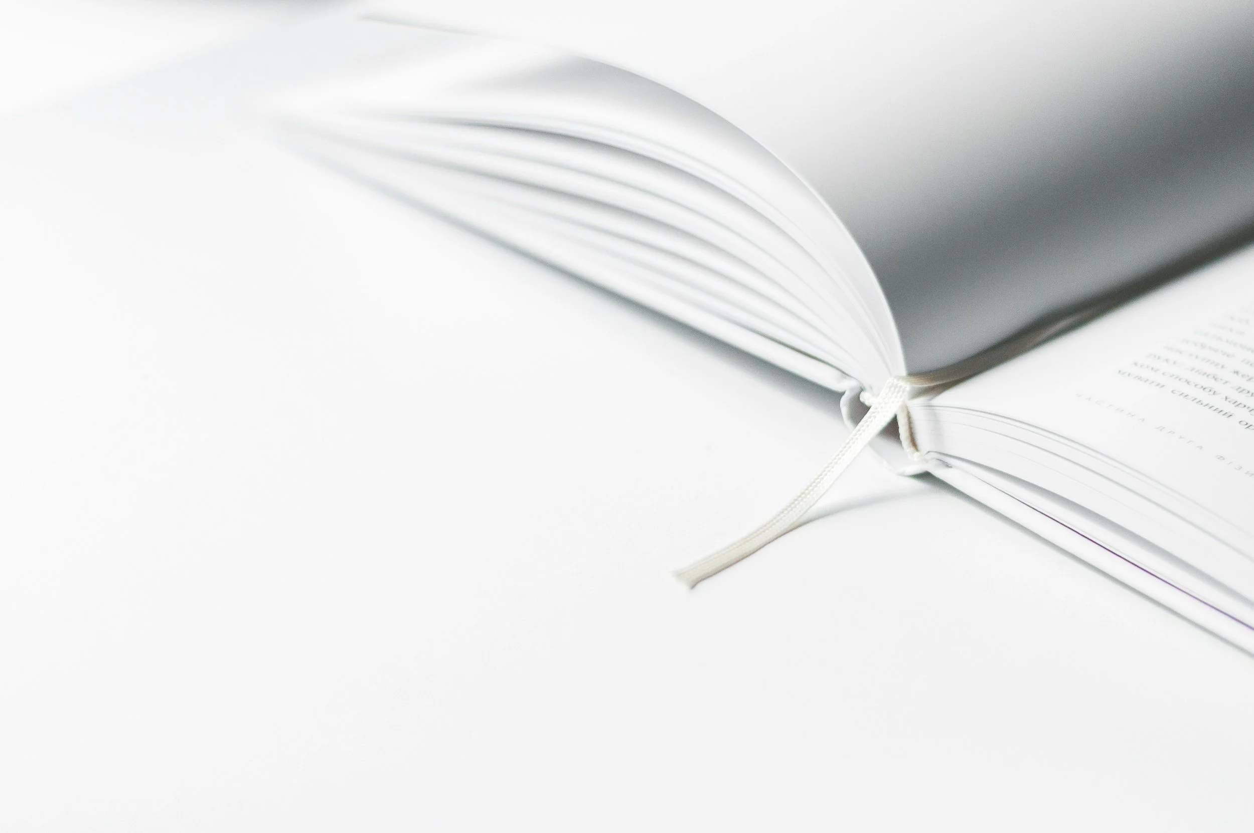 Open white notebook with blank pages and a white ribbon bookmark on a white surface.