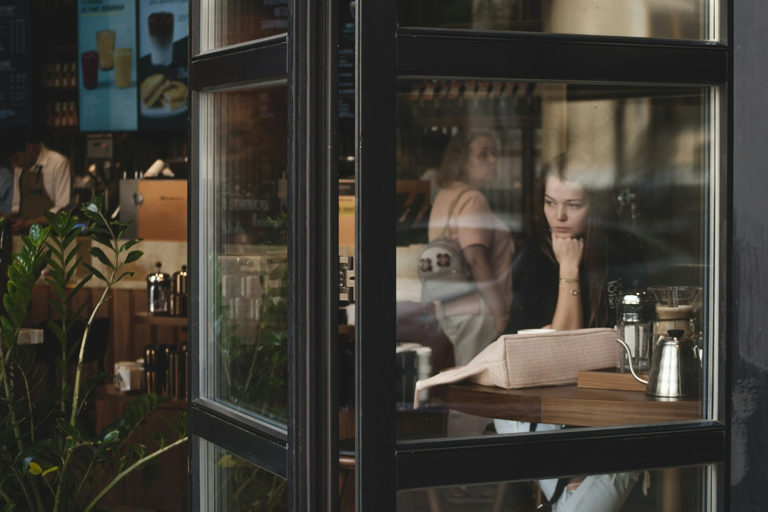 Thoughtful adult sitting in a café reflecting on a recent conversation, representing social anxiety and overthinking social interactions.