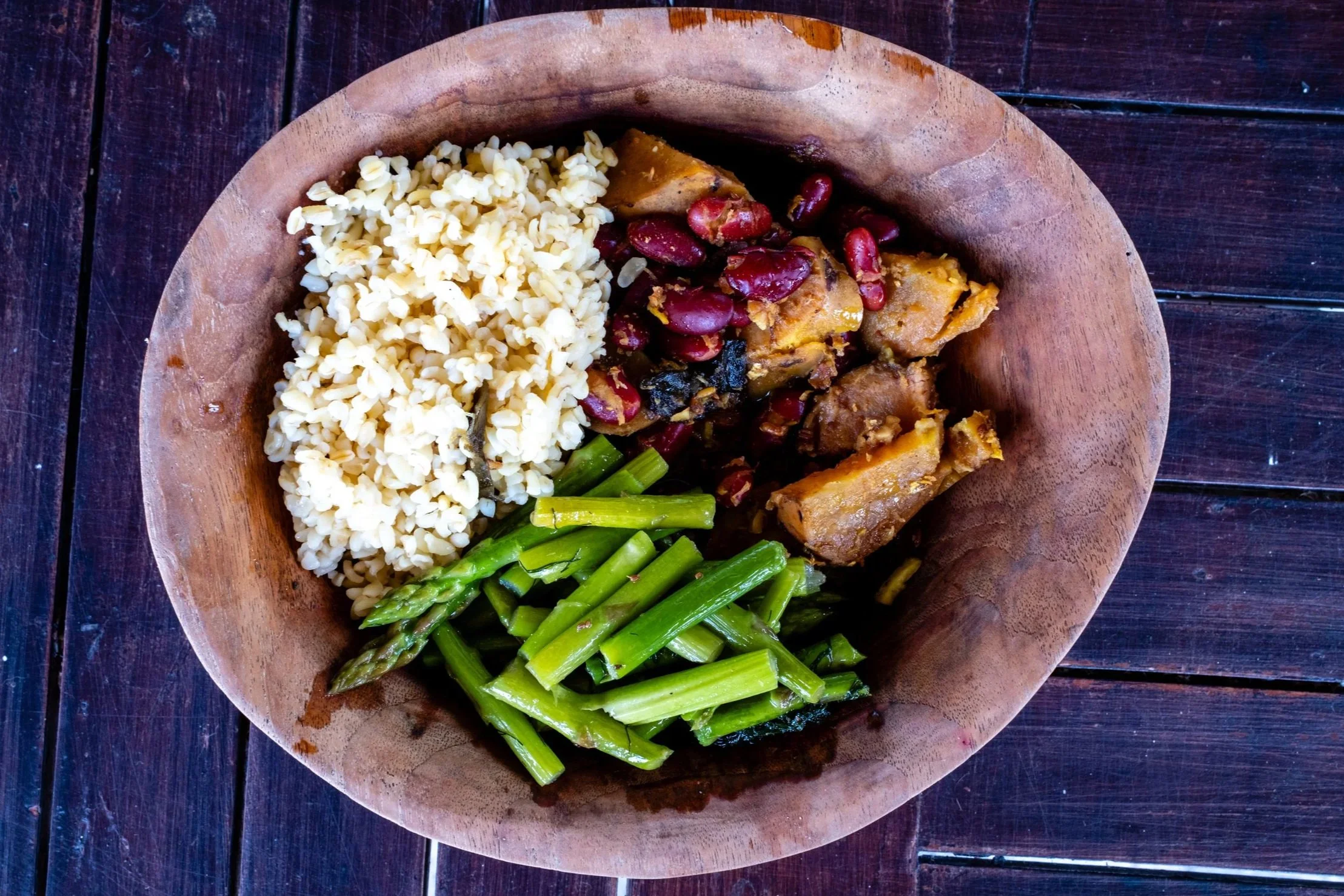 A wooden bowl containing cooked rice, green vegetables, beans and sweet potatoes.