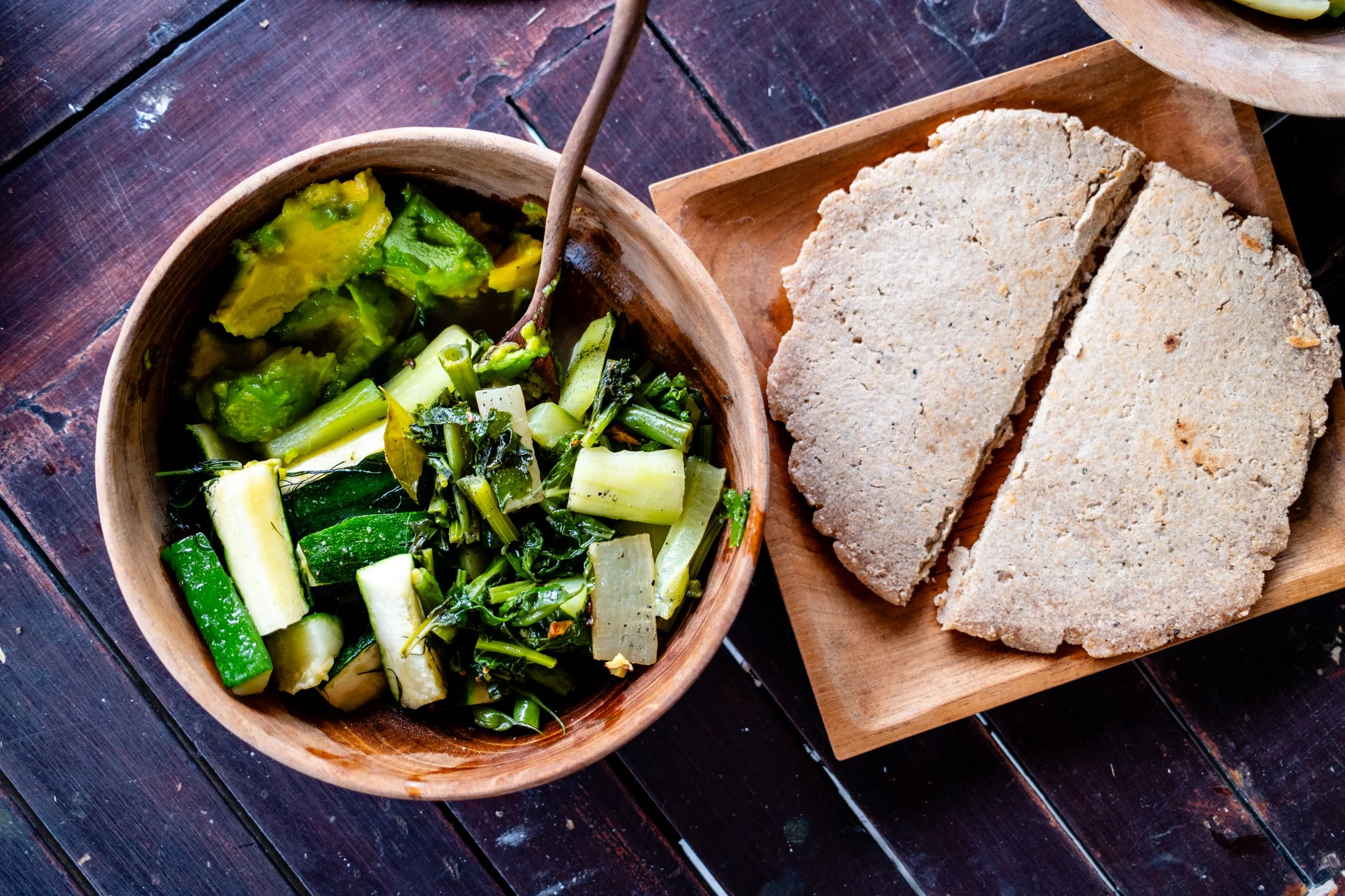 Green vegetable stew in a wooden bowl and slices of bread on a wooden tray.