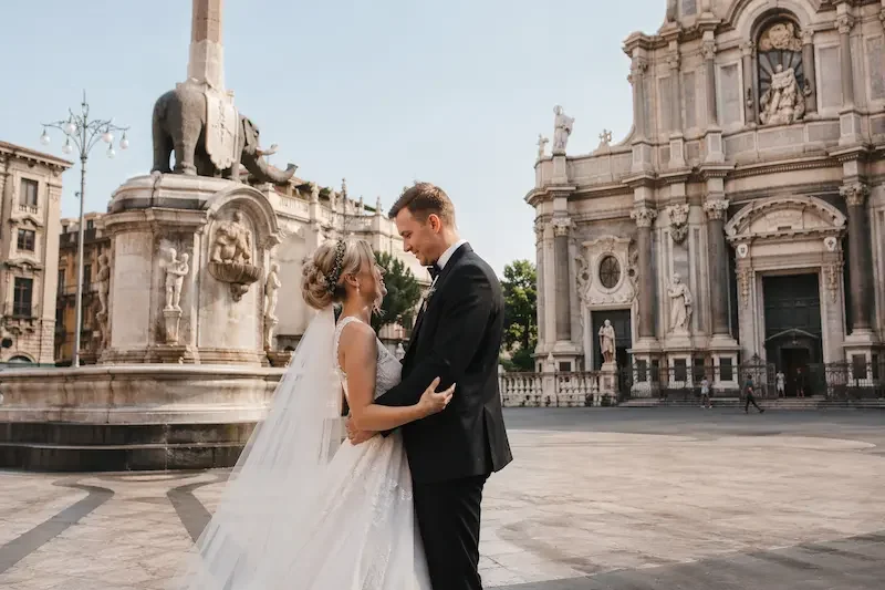 American couple during destination wedding photo session in Piazza Duomo Catania Sicily with Liotro Fountain and Saint Agatha Cathedral, luxury wedding in Italy for US and UK couples