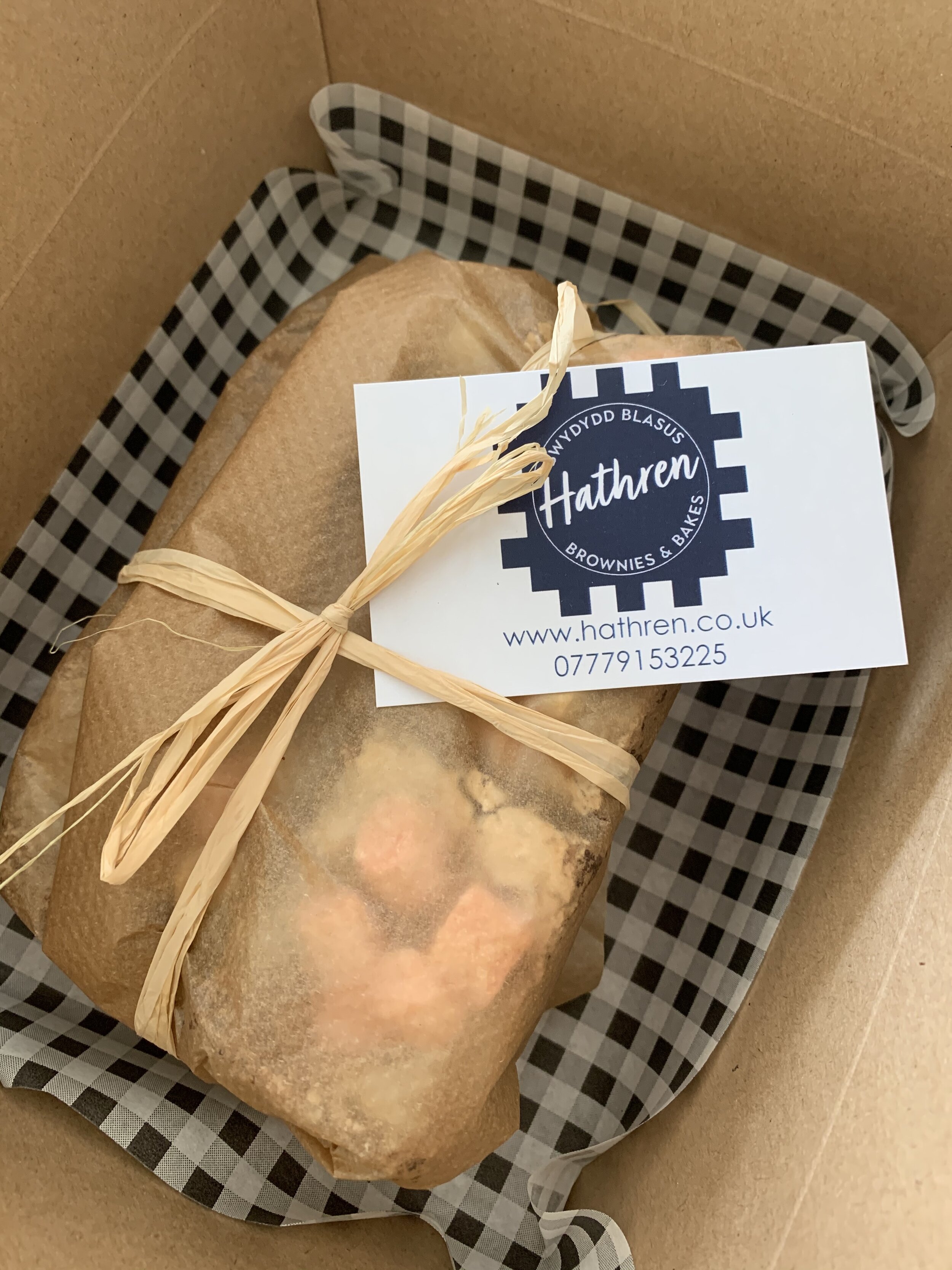 A paper-wrapped package tied with raffia, inside a box lined with black and white checkered paper. It has a business card from Hathren with contact information.