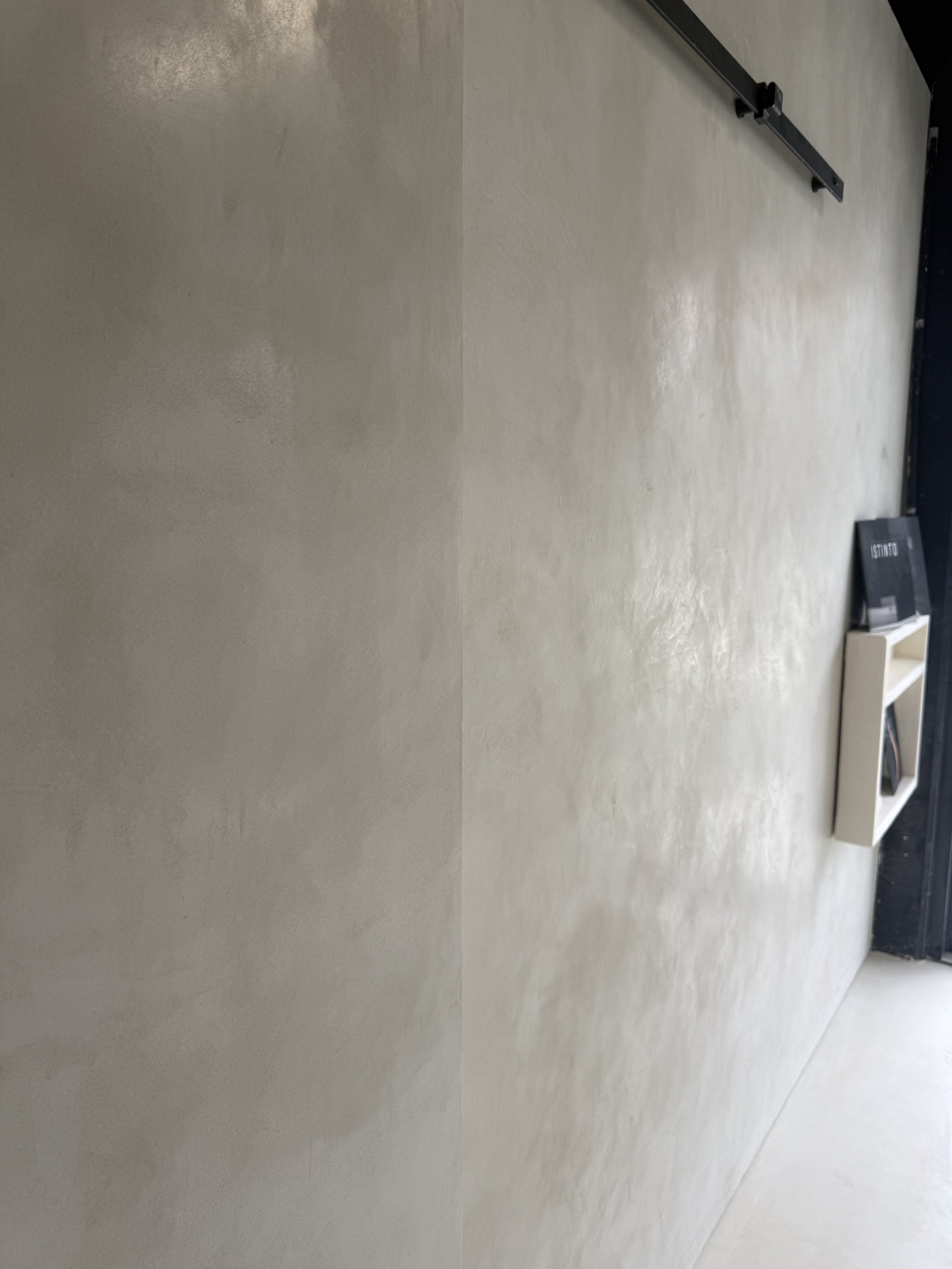 A beige wall with a black sliding door rail system and a small black shelf holding a book titled 'STAND.'
Otsumigaki Japanese Polsihed Plaster finish Mornington Peninsula