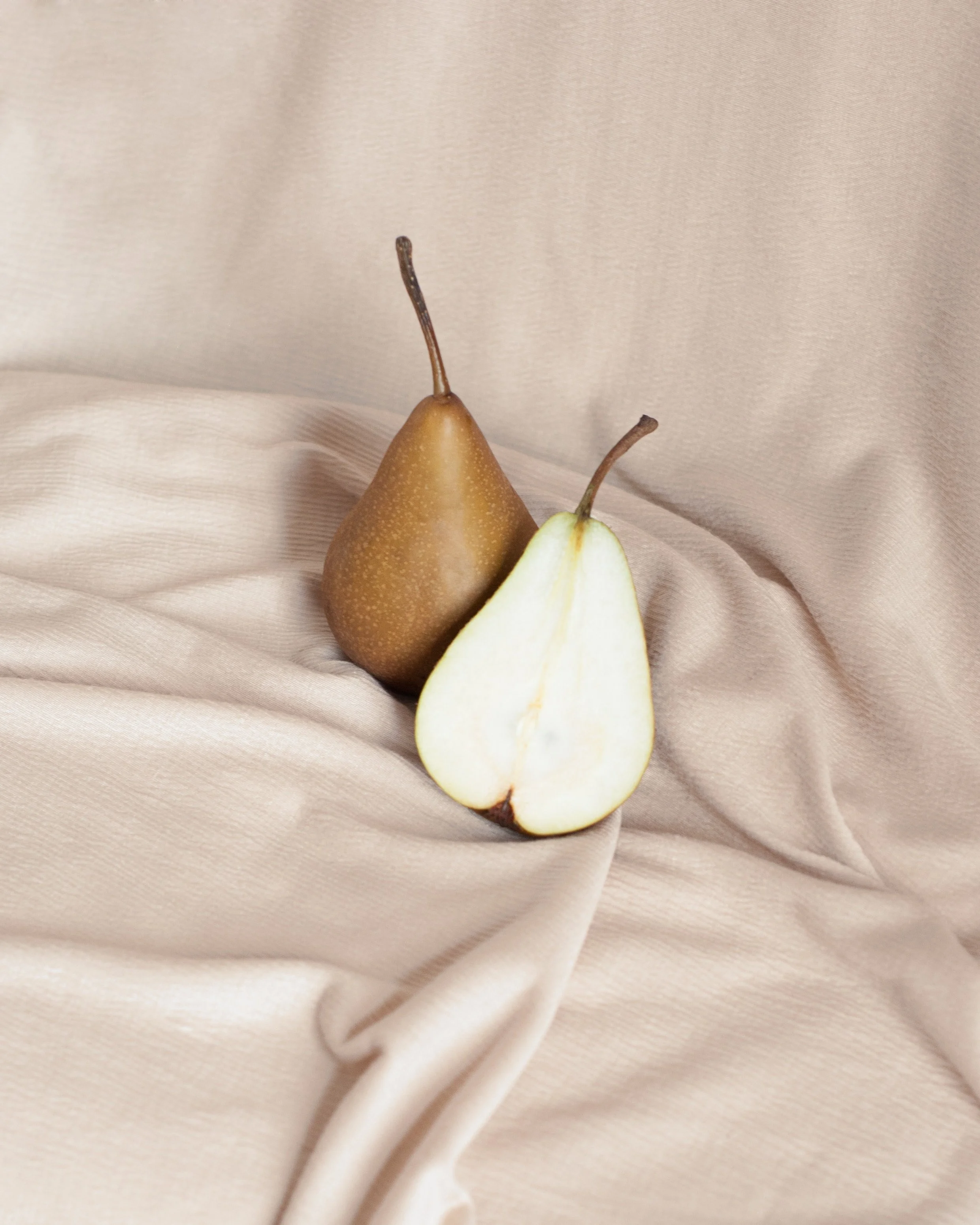 A whole pear and a halved pear on beige fabric.