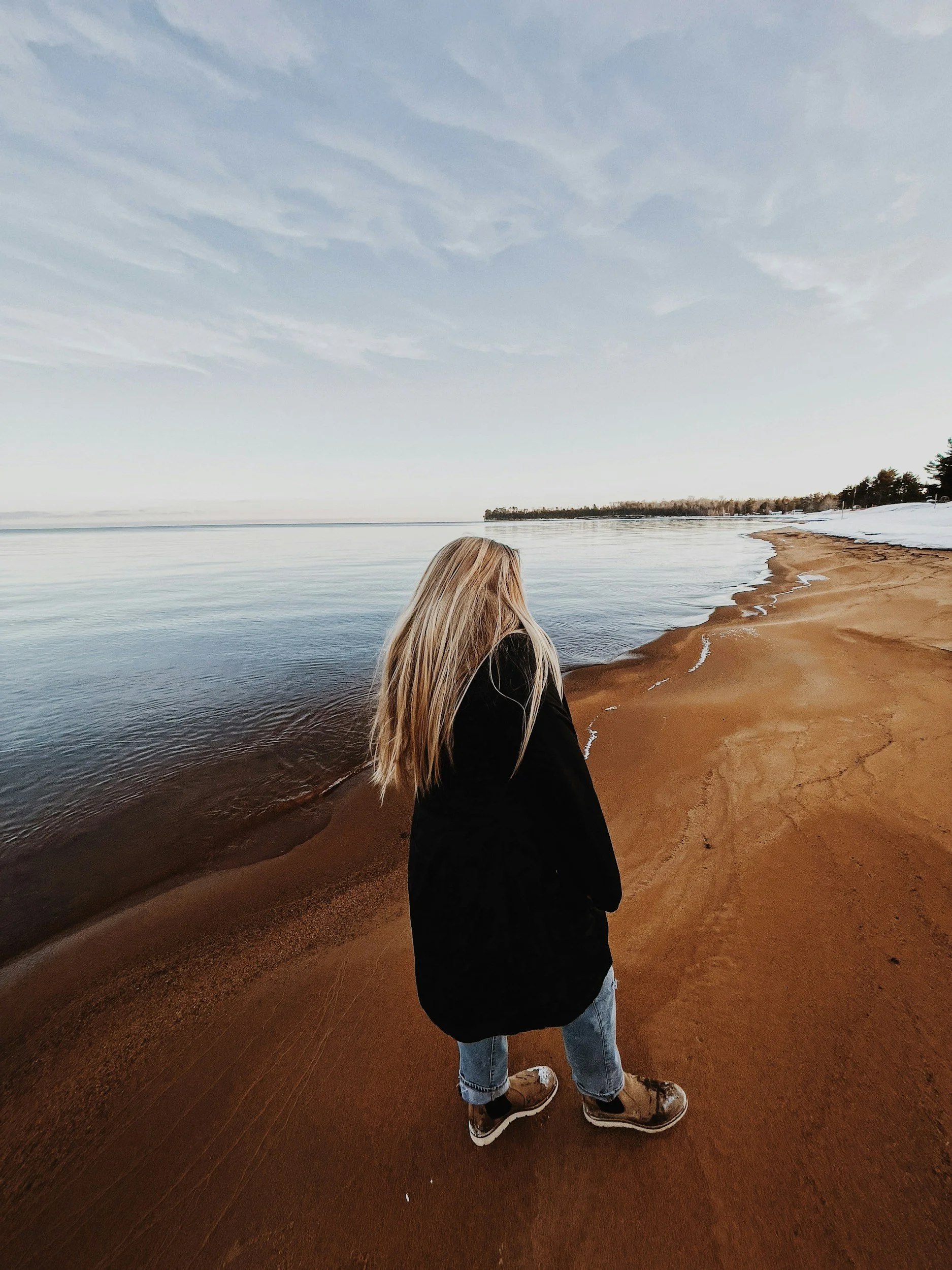 Woman standing on sandy beach besides the water.