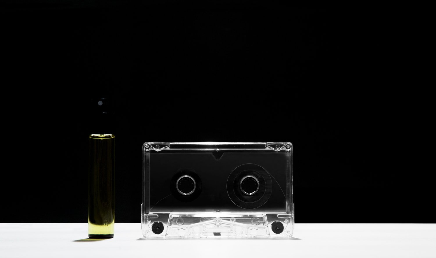 A clear cassette tape and a black and yellow battery placed on a white surface against a black background.