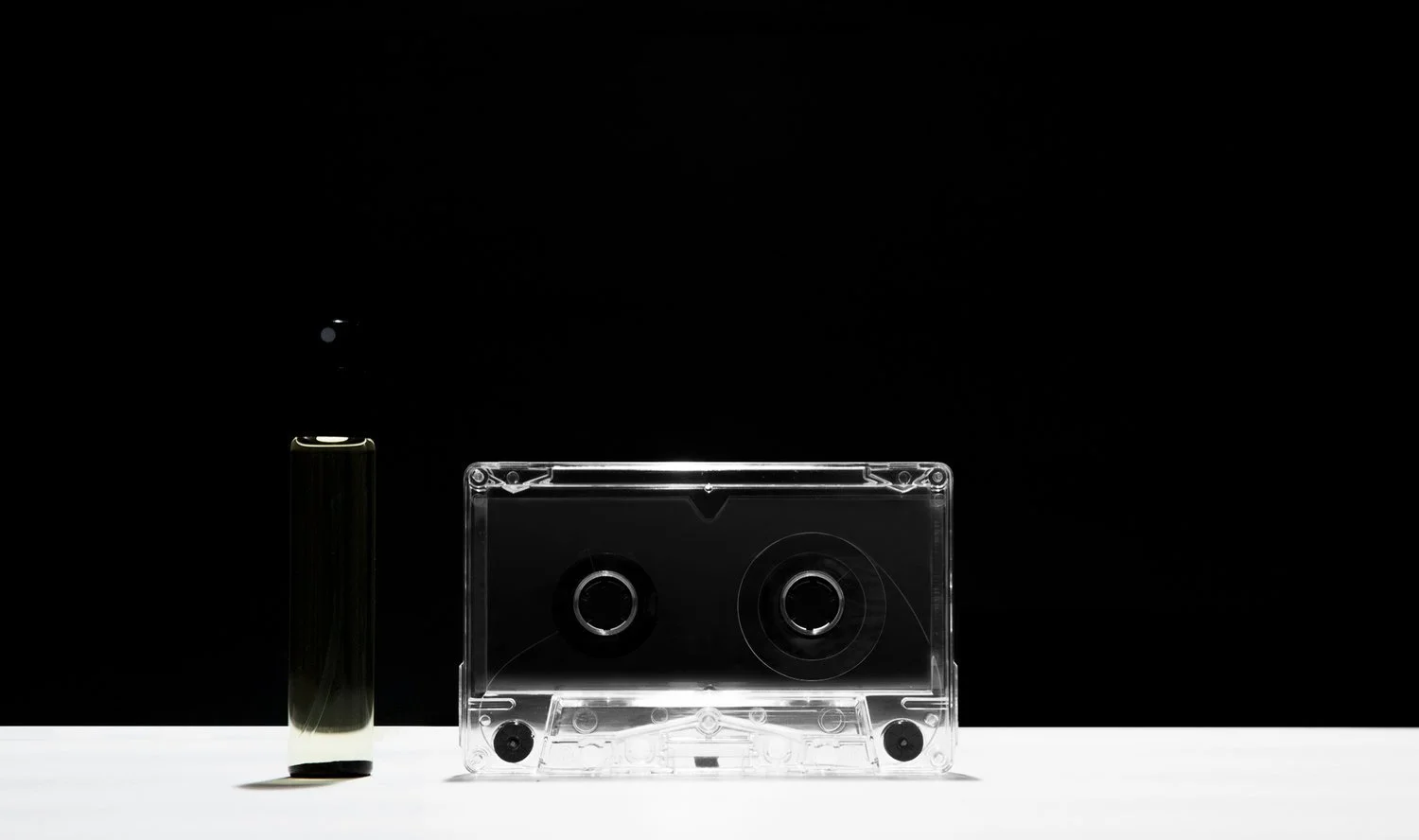 A black vape pen stand on the left and a clear cassette tape on the right, placed on a white surface with a black background.