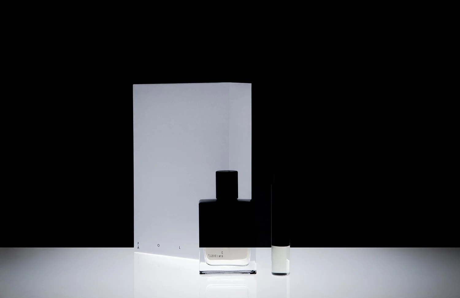 Three minimalist bottles, one large white and black bottle with a black cap, one small black and white bottle with a black cap, and one small white bottle, arranged on a white surface with a black background.