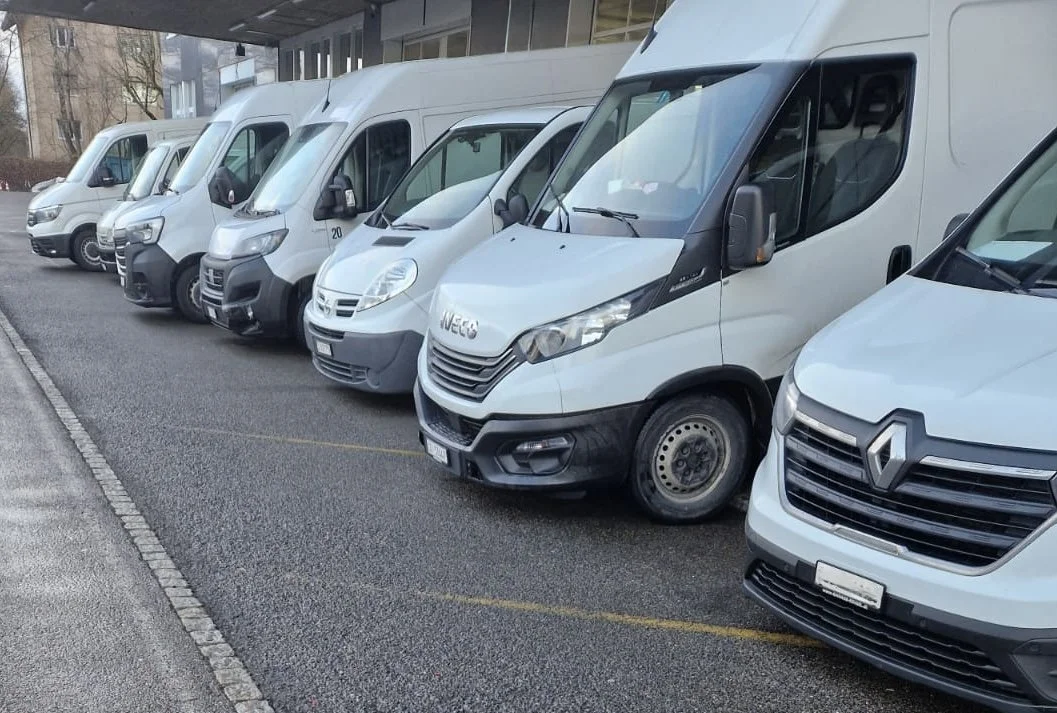 Mehrere weiße Lieferwagen sind nebeneinander in einer Parkreihe parkend.