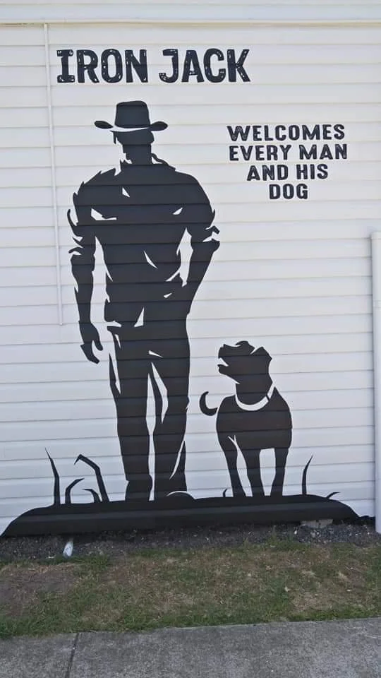 Silhouette of a man wearing a cowboy hat walking with his dog on a grassy field, with text that says 'Iron Jack welcomes every man and his dog.'
