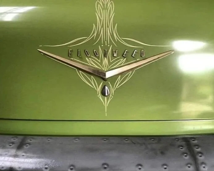 Close-up of a vintage green car hood ornament with the word 'FLOWFEED' and a decorative emblem in the center.