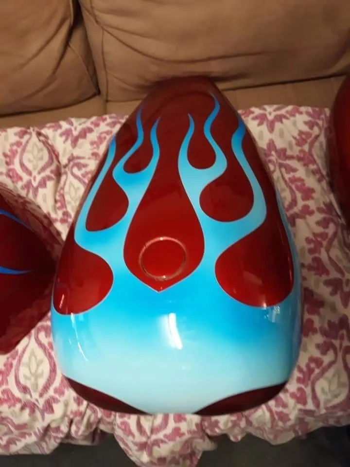 A skateboard deck with a flame design in red, blue, and white colors resting on a pink and white patterned blanket.