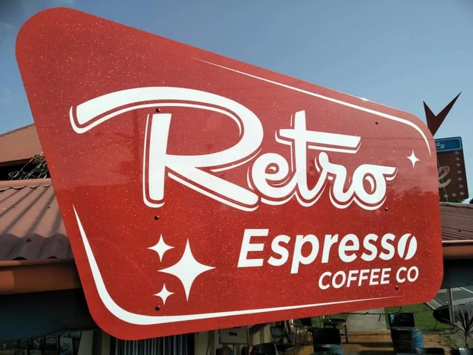 Red retro-style coffee shop sign with white lettering that says 'Retro Espresso Coffee Co' under a clear blue sky.