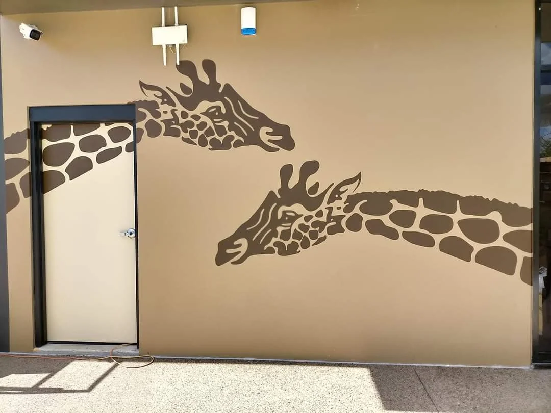 Wall with a mural of two brown giraffe heads facing each other, on a beige background.