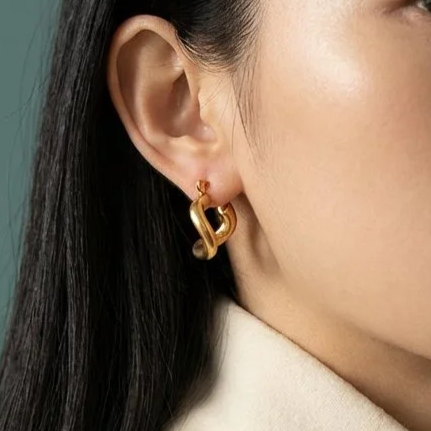 Close-up of a woman's ear with a gold earring in the shape of a hammer.