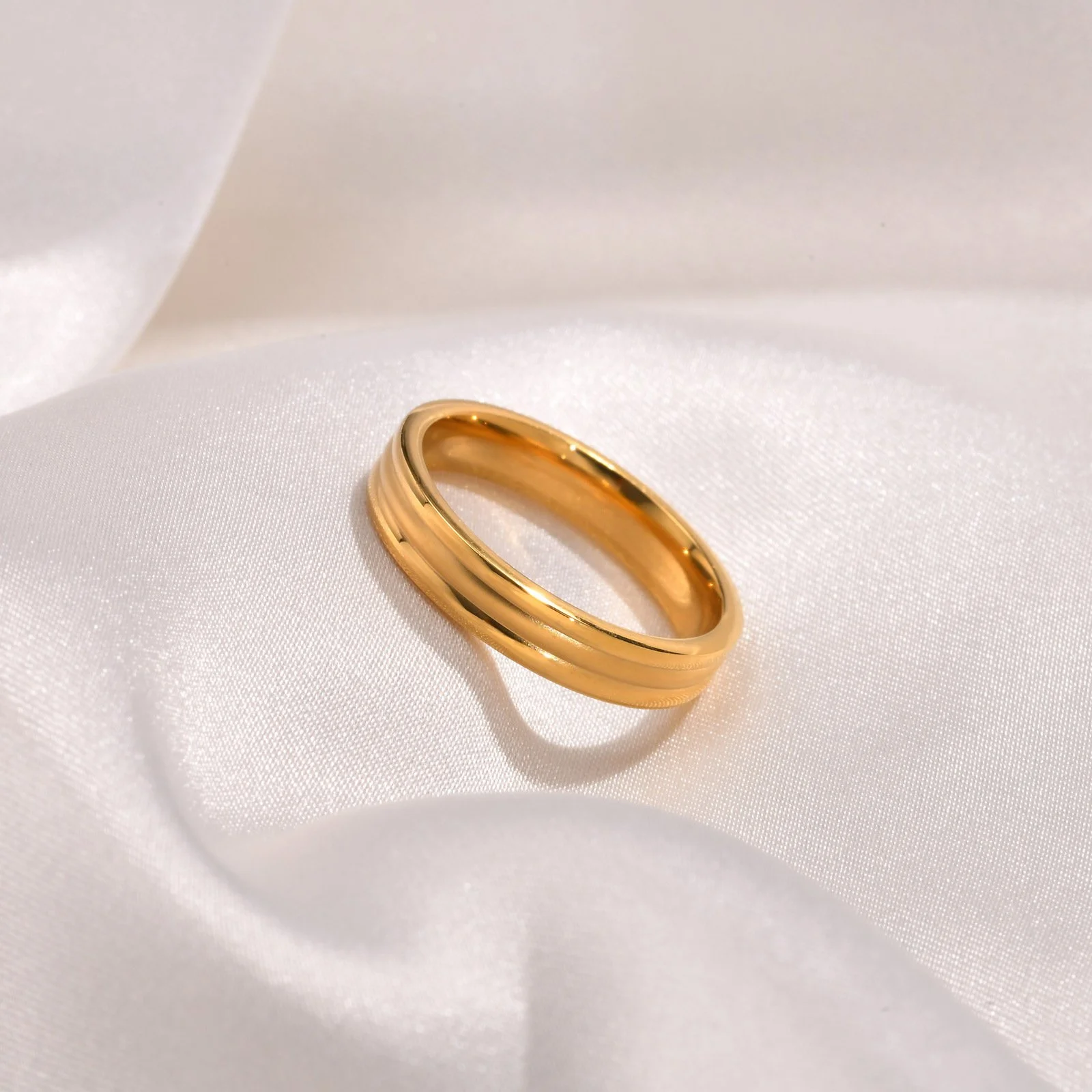 A gold ring with a polished finish resting on white satin fabric.