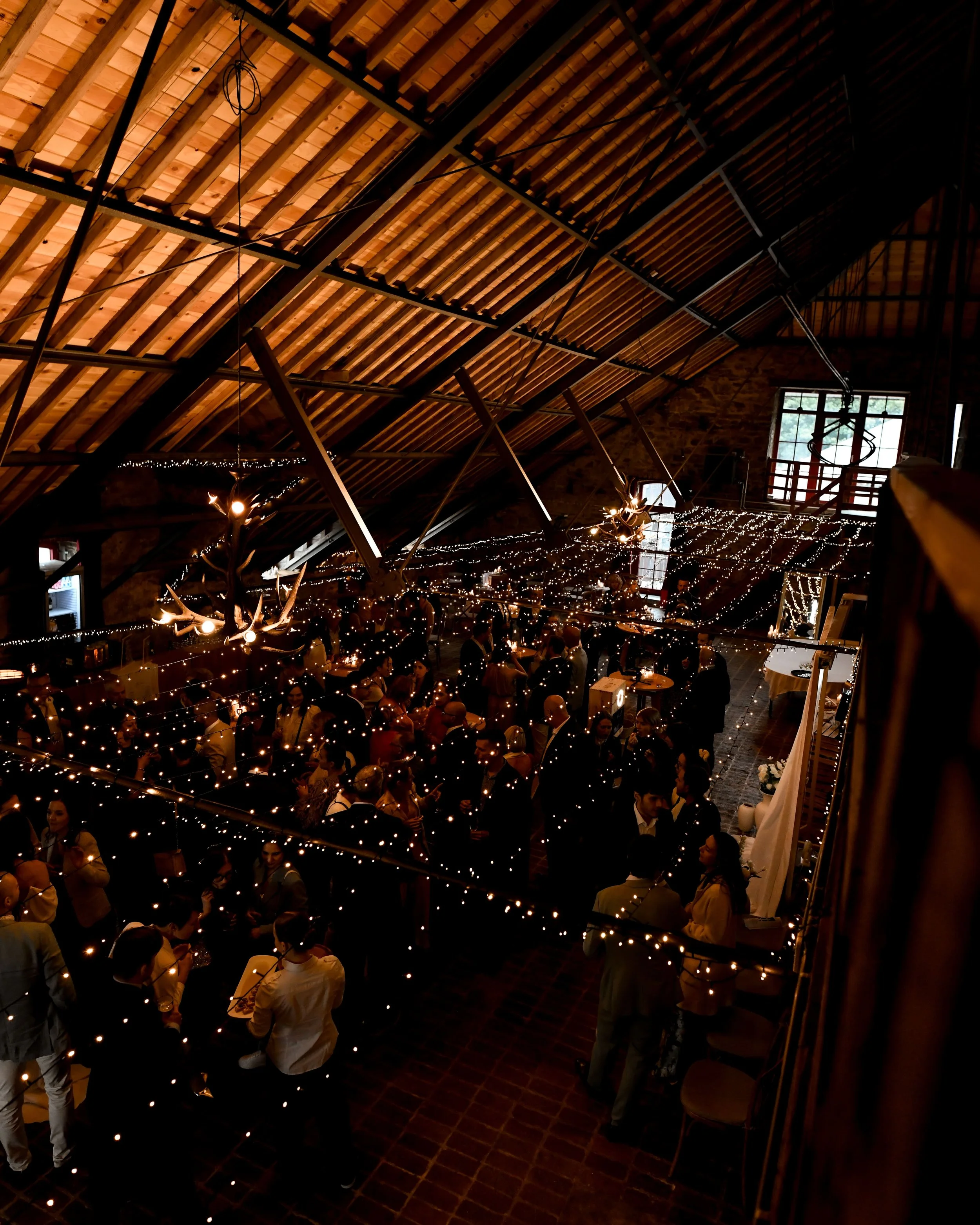 Une salle avec un plafond en bois, décorée avec des guirlandes lumineuses, où des personnes se rassemblent pour un événement ou une fête dans une ambiance chaleureuse.