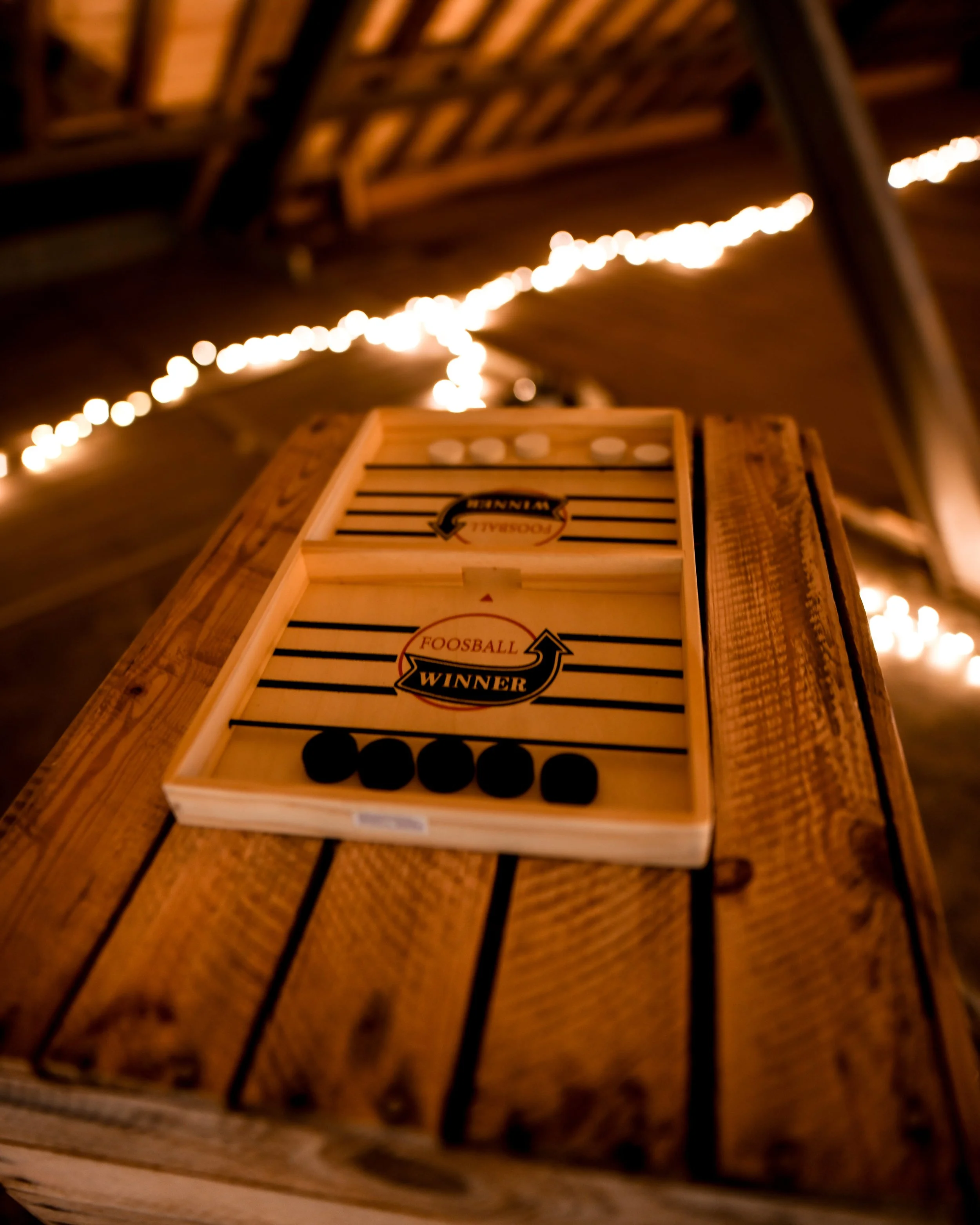 Une boîte de jeu de fléchettes en bois sur une table en bois, avec un panneau « Winner » et des points noirs.