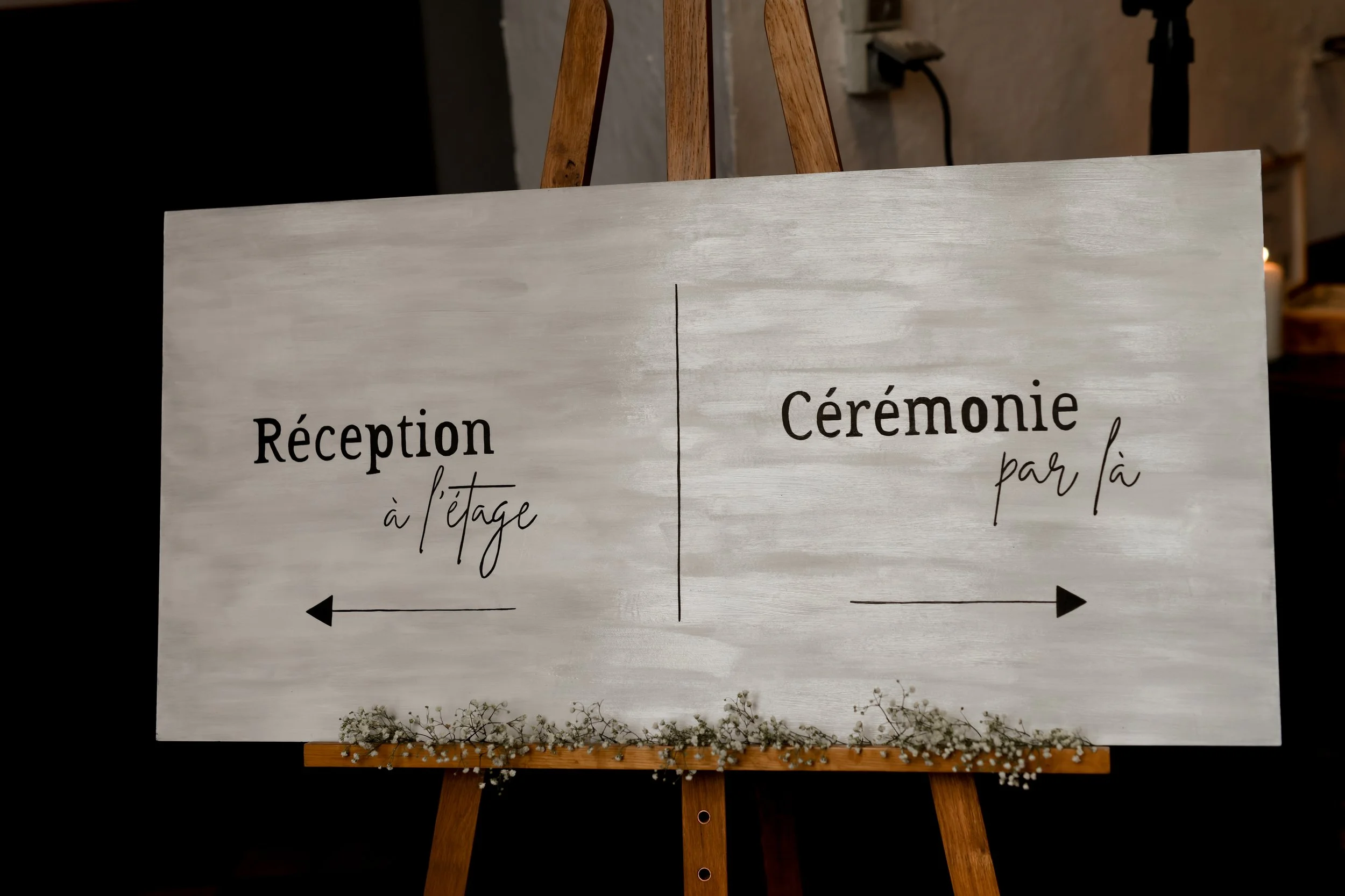 Panneau indiquant l'accueil à l'étage à gauche et la cérémonie par là à droite, décoré avec des petites fleurs blanches en bas.