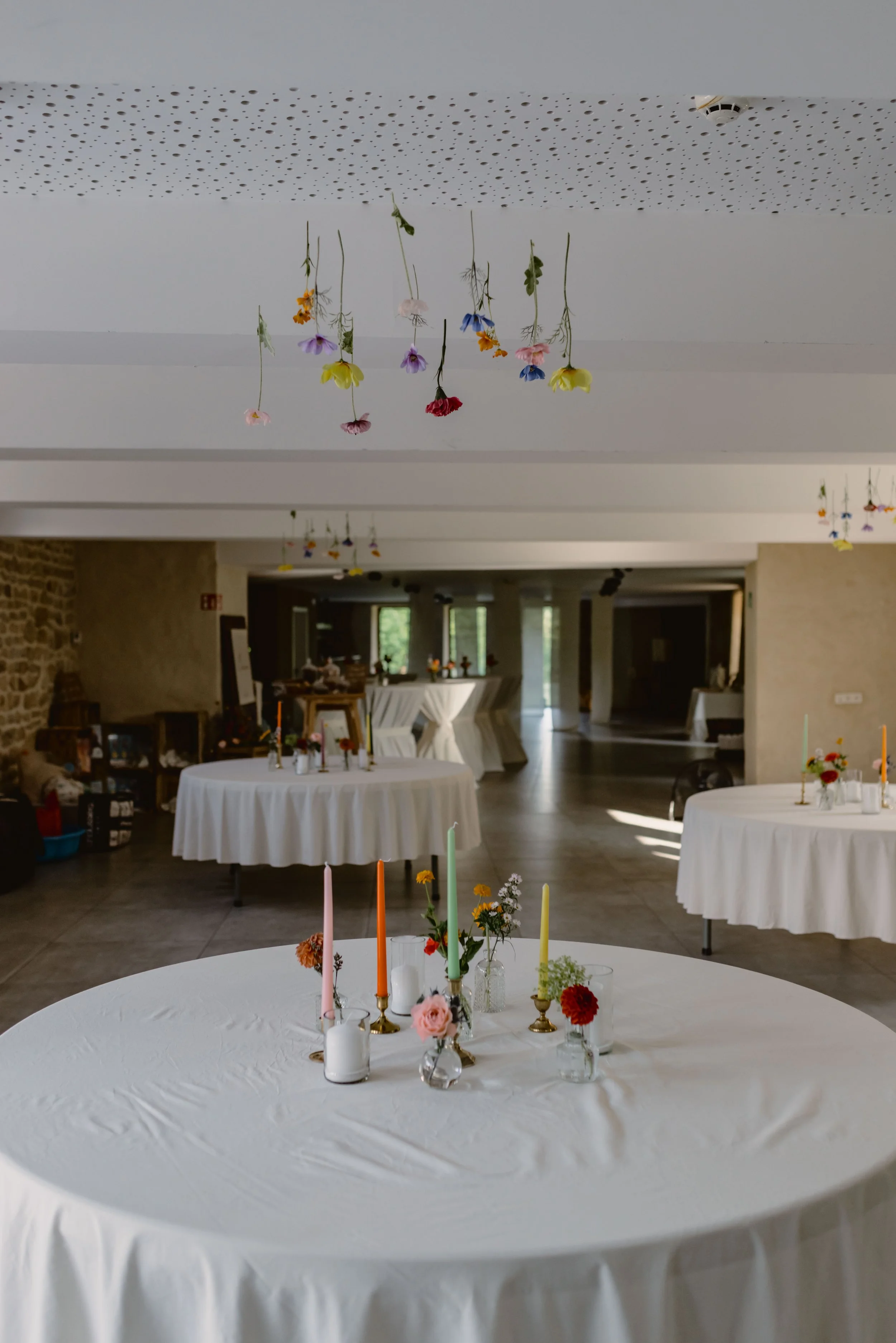 Une salle de réception décorée avec des tables rondes recouvertes de nappes blanches, ornées de vases avec des fleurs et des bougies, pour une occasion spéciale.