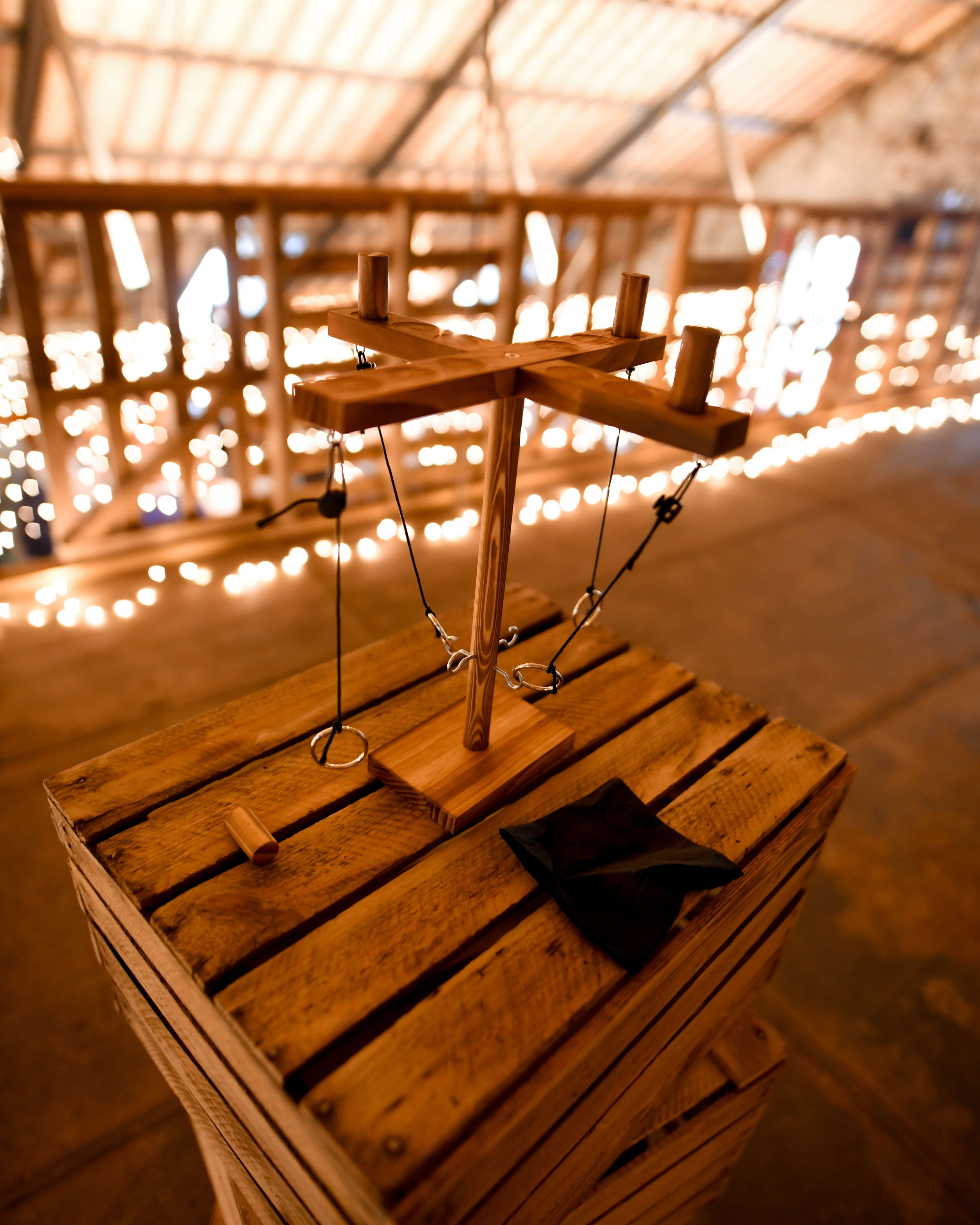 Une structure en bois suspendue avec des fils, dans un éclairage tamisé et un fond flou illuminé de lumières chaudes.