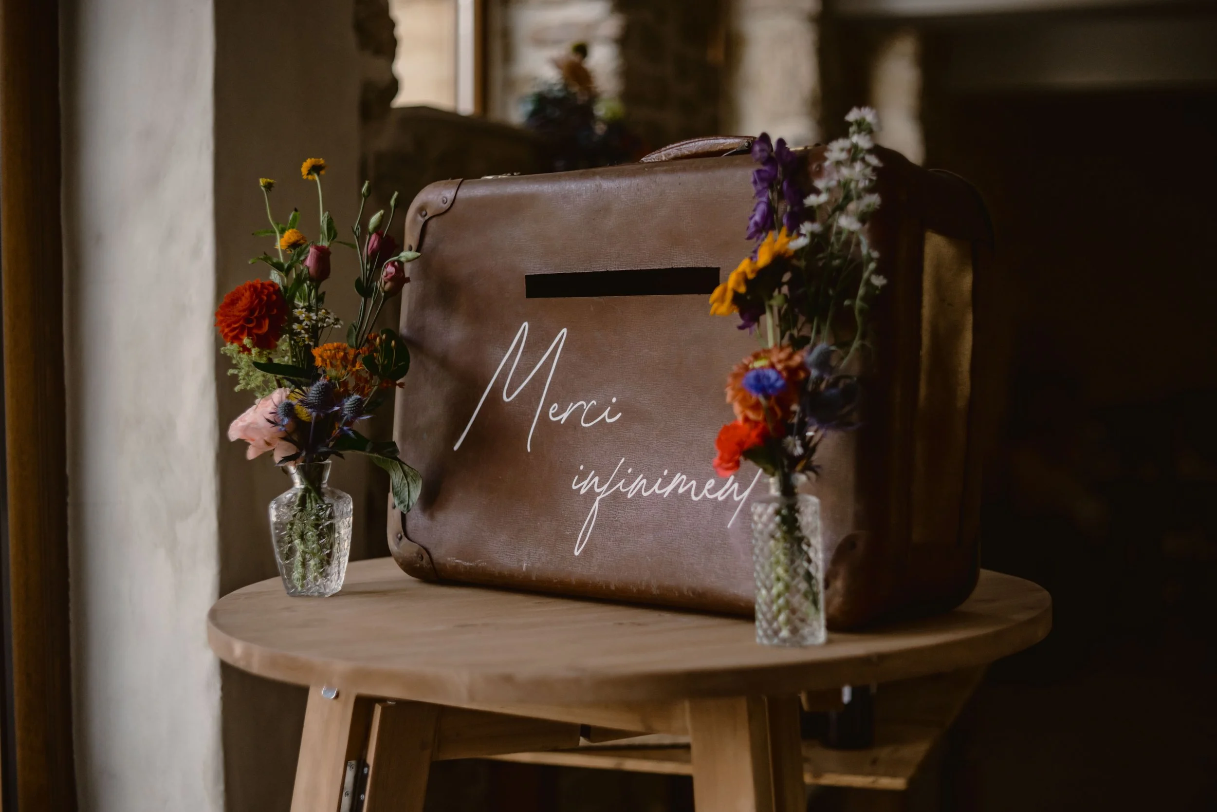 Arrangements floraux dans des vases en verre, décorant une table avec un panneau en toile marron avec le mot 'Merci' écrit en blanc, dans un cadre intérieur chaleureux.