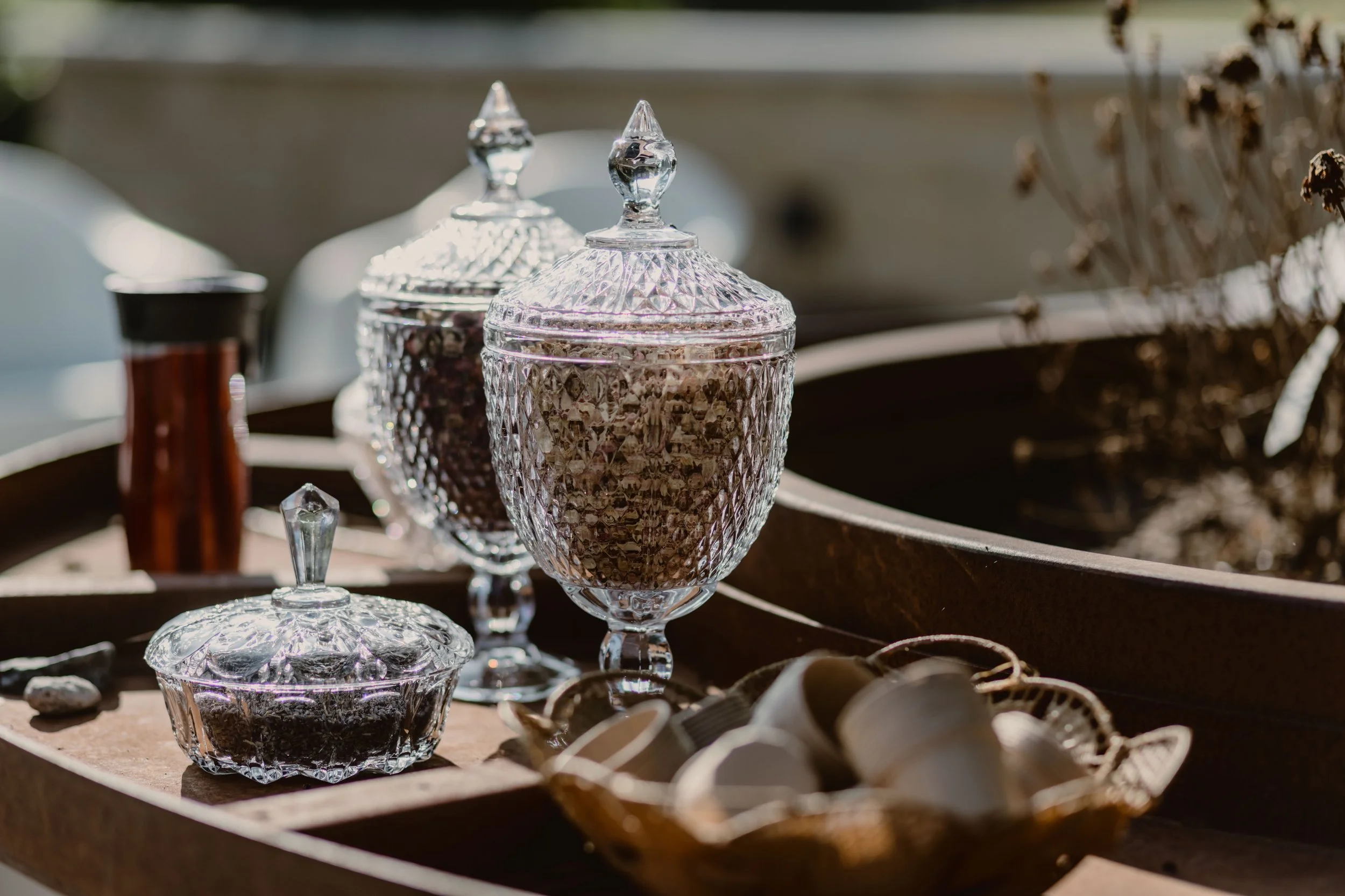 Des pots en cristal contenant des pétales de fleurs, exposées sur une table en métal, avec d'autres objets décoratifs en arrière-plan.